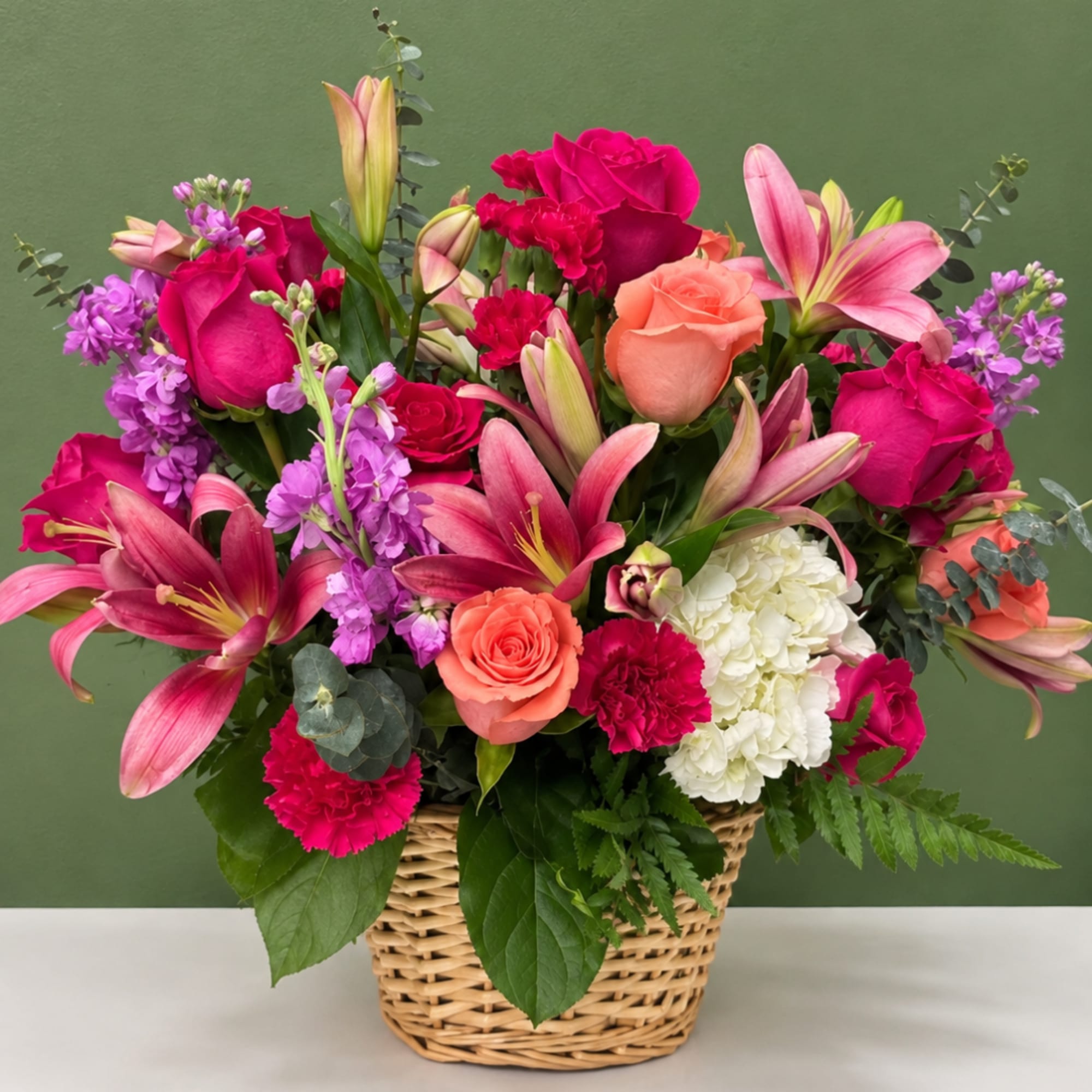 Mixed bouquet in a wicker basket with pink lilies, roses, carnations, and hydrangea