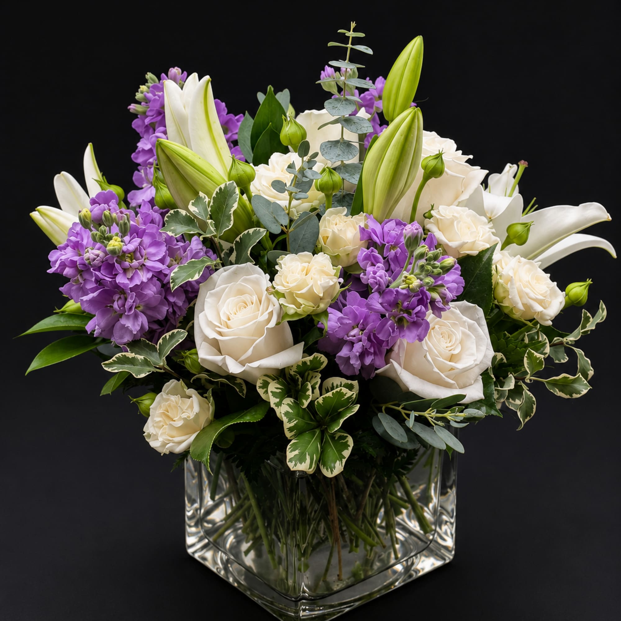 White roses and purple stock arranged in a clear square vase