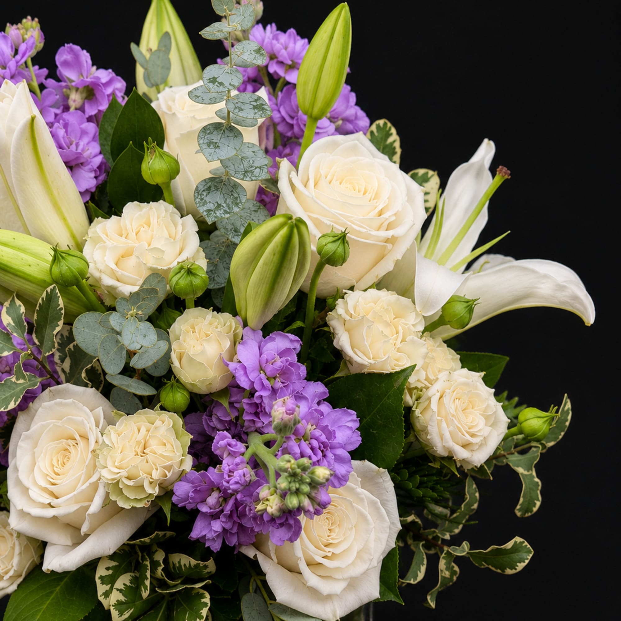 White roses and lilies with purple flowers in a glass vase