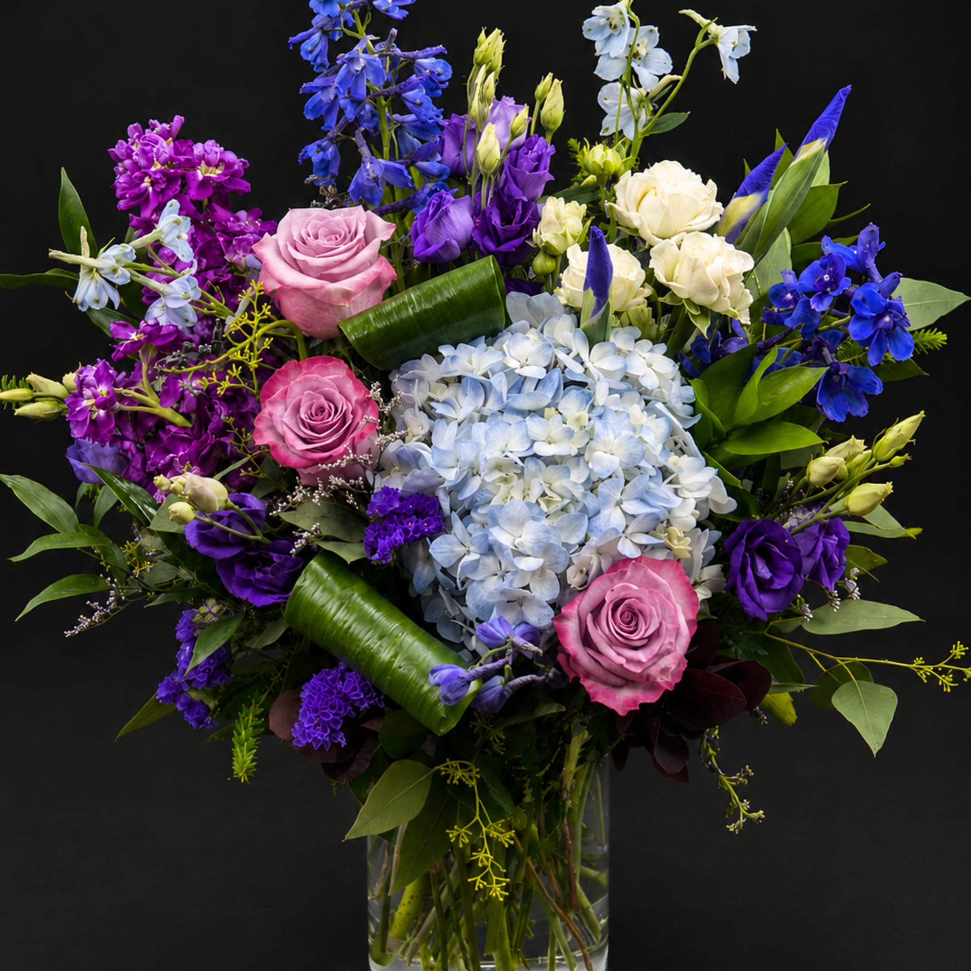 Mixed bouquet of roses, hydrangea, and purple blooms in a glass vase