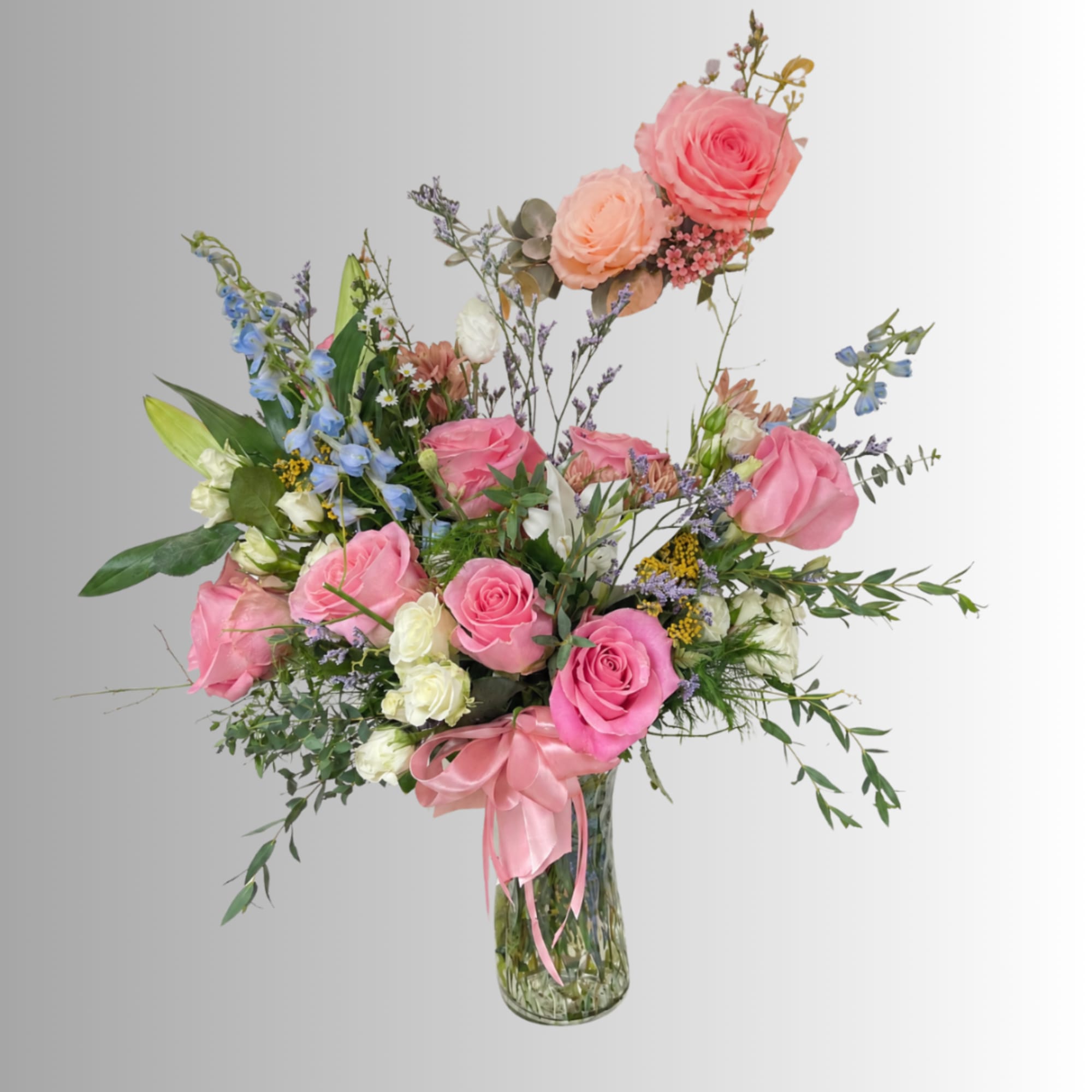 Pink and peach roses in a clear glass vase with a pink ribbon