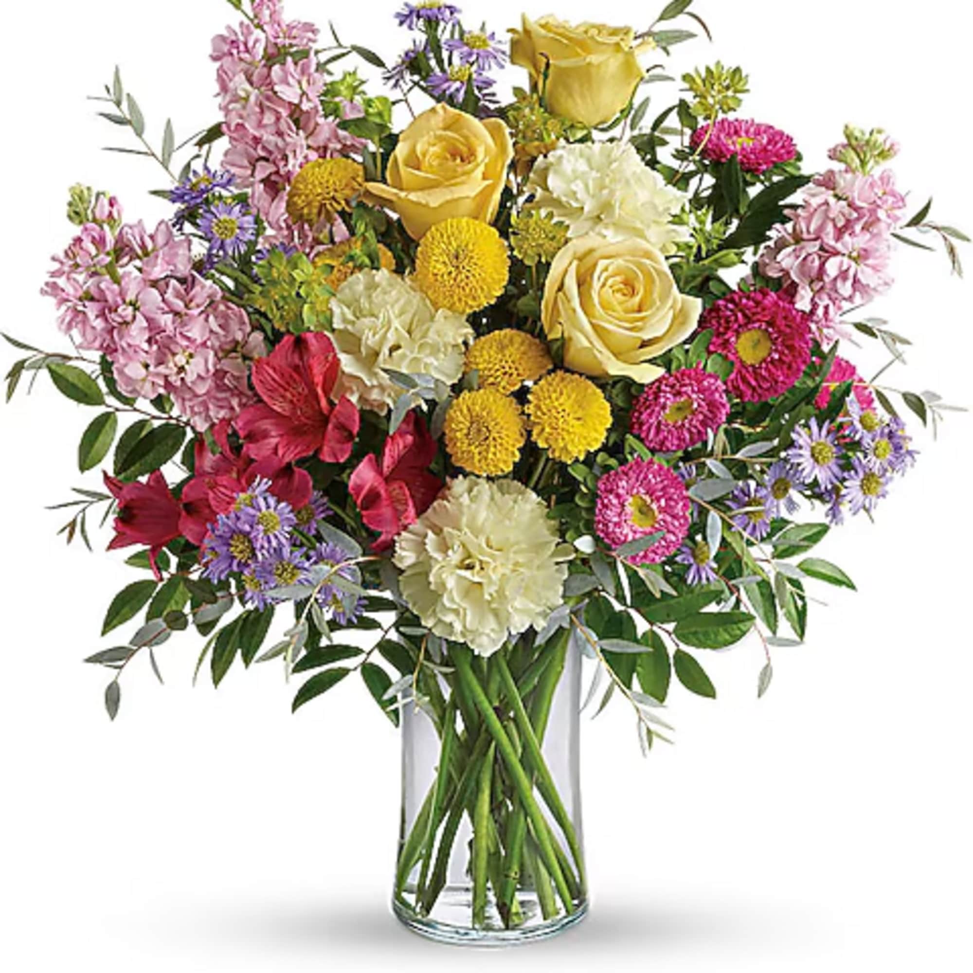 Mixed bouquet of yellow roses, pink blooms, and purple daisies in a glass vase