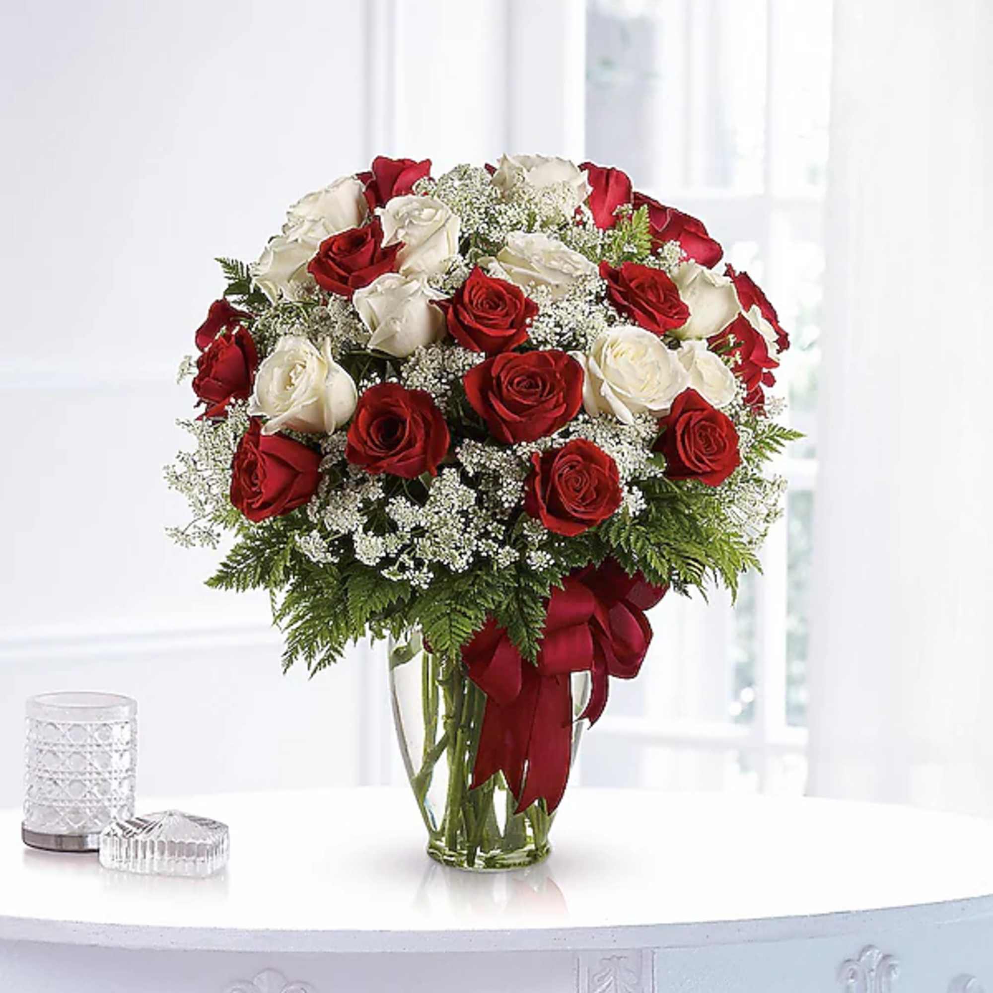 Red and white roses in a clear glass vase with a red ribbon