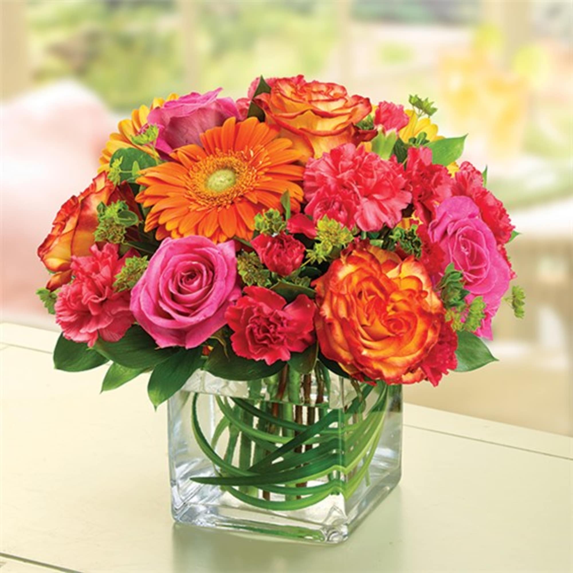 Mixed bouquet of pink, orange, and red flowers in a clear glass vase