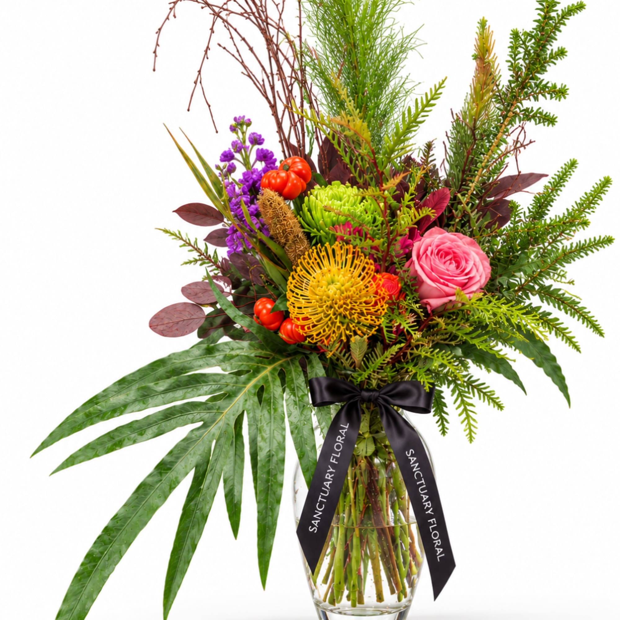 Tropical bouquet with pink rose, yellow pincushion bloom, and purple flowers in a glass vase