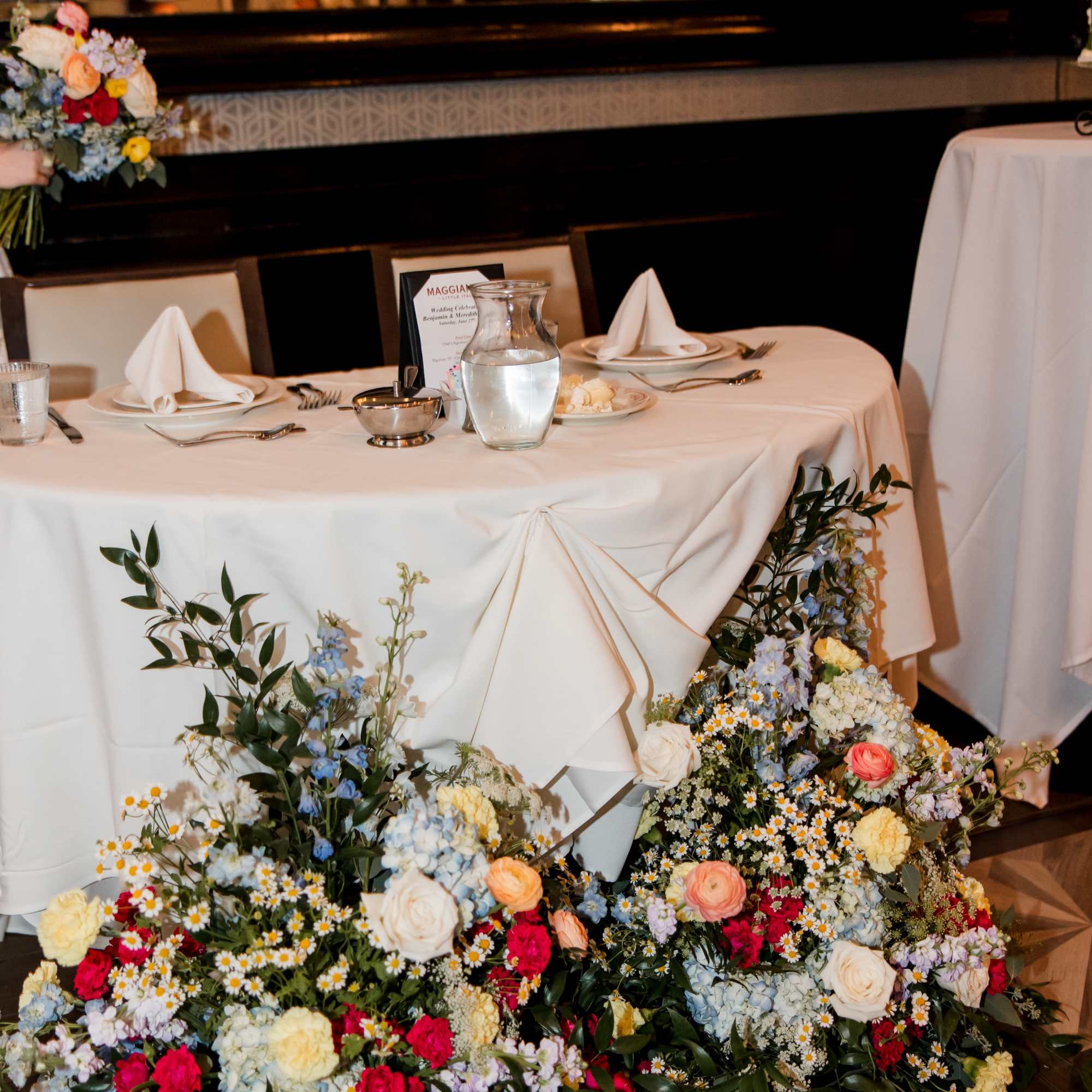 Floral arrangement around a draped table with white napkins and glassware