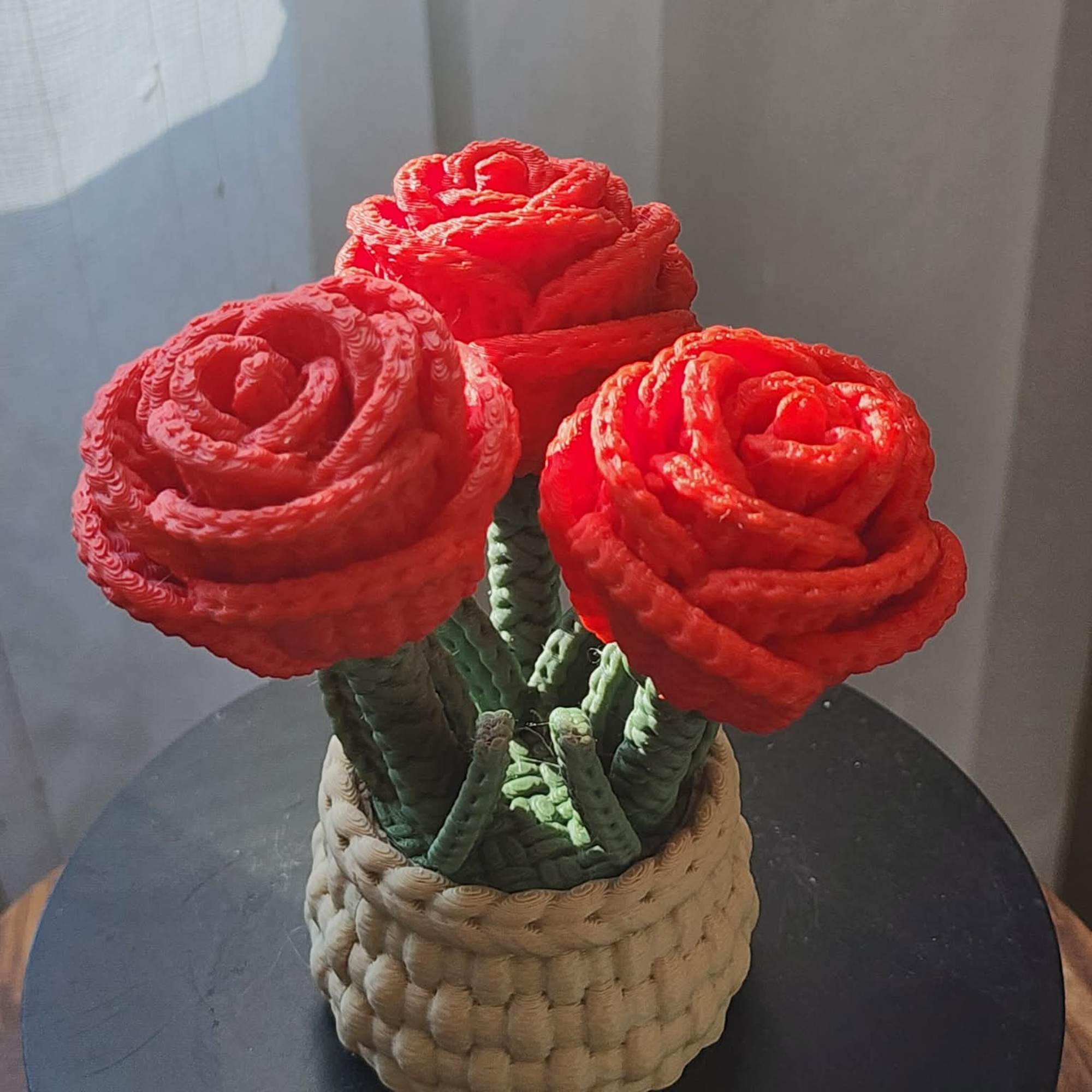 Three red rose-shaped flowers in a woven basket container