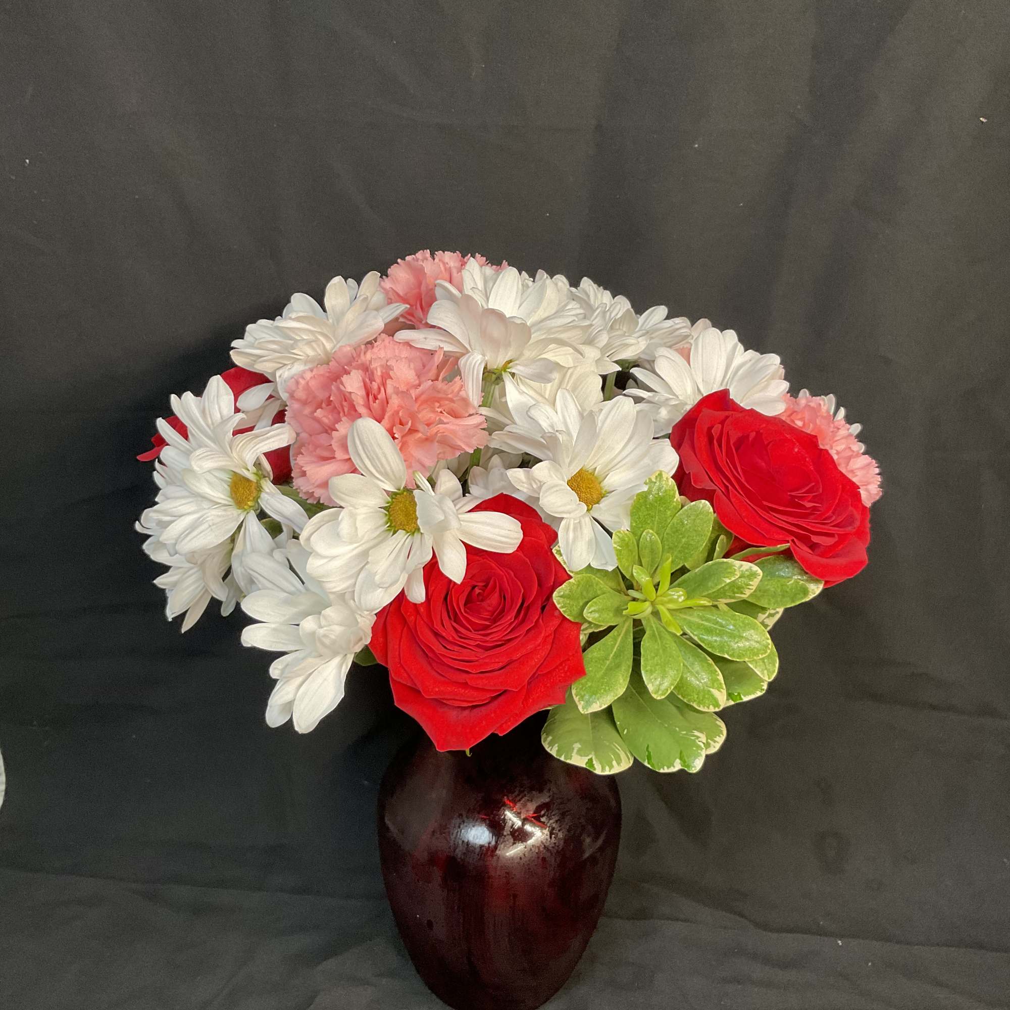 Bouquet of red roses, white daisies, and pink carnations in a dark vase