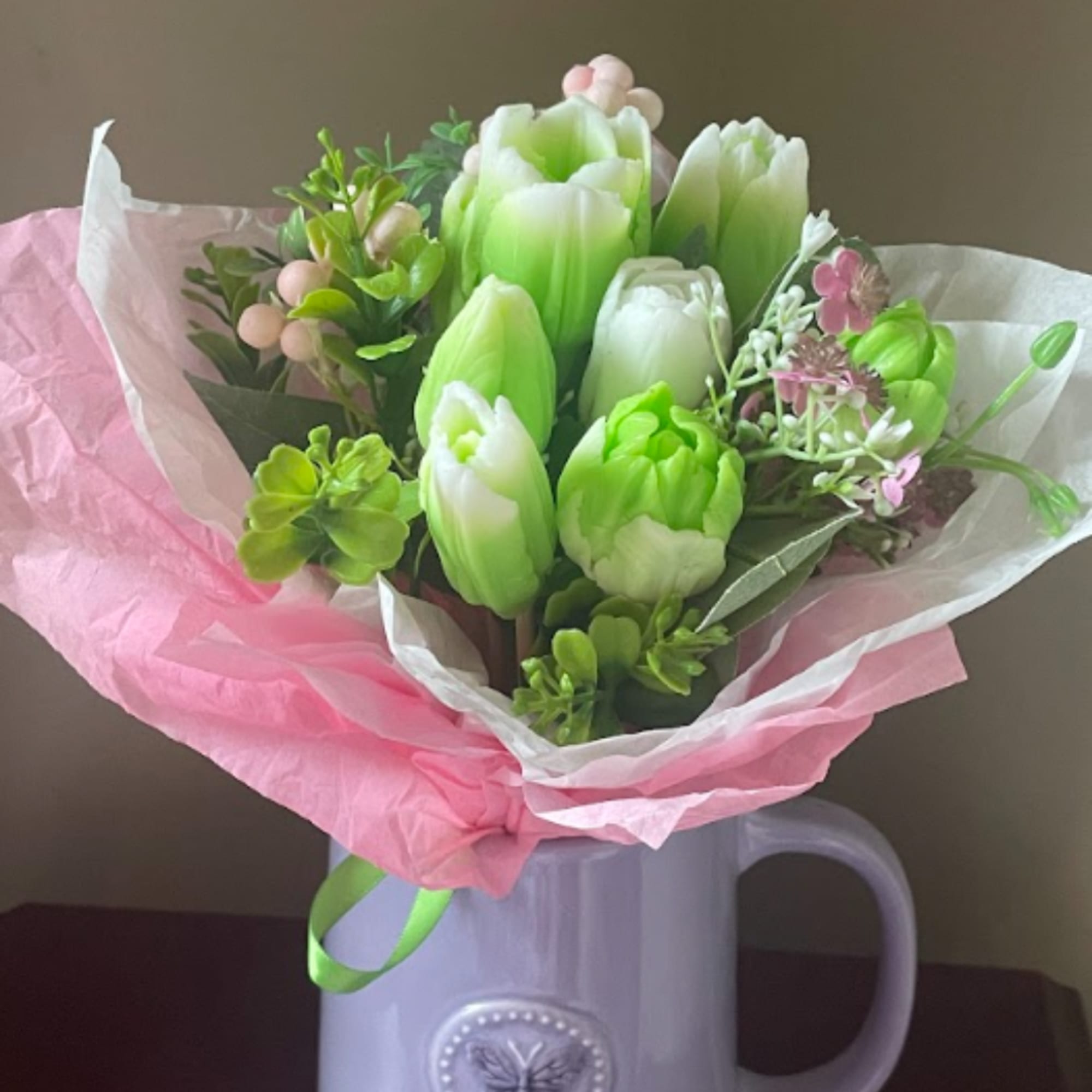 Green and white tulip bouquet wrapped in pink paper in a lavender mug