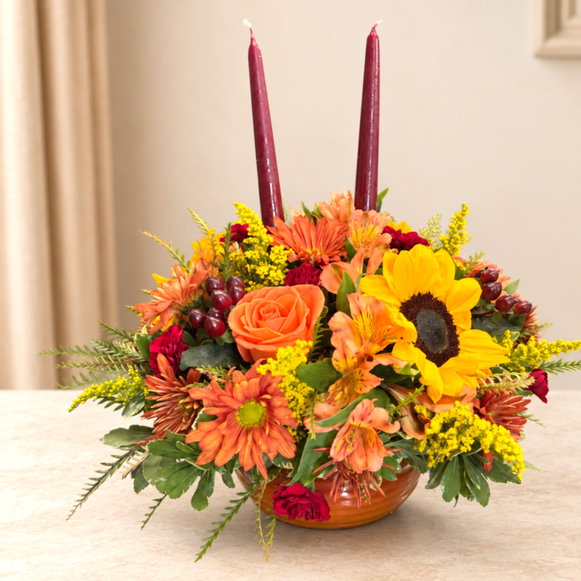 Autumn floral centerpiece with sunflowers, roses, and two burgundy candles in a low bowl