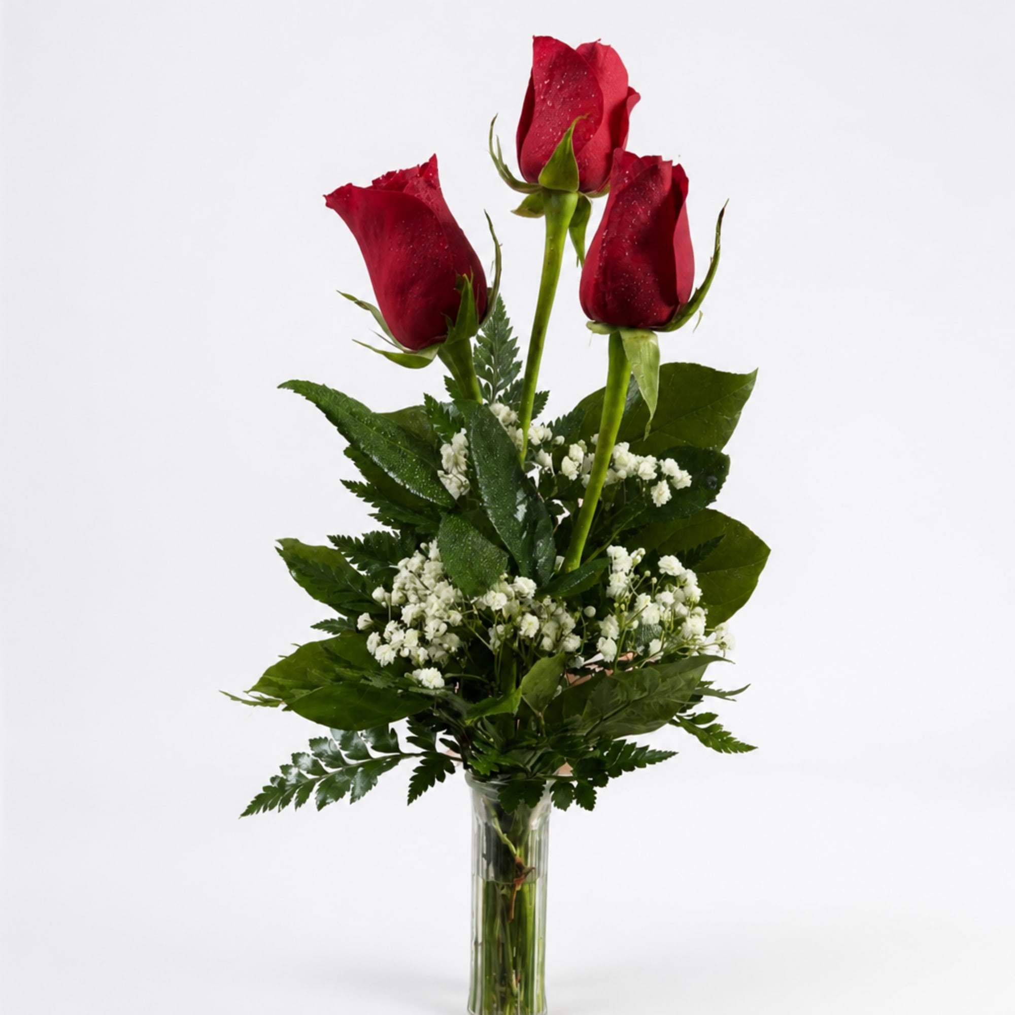Three red roses in a clear glass vase with white filler flowers
