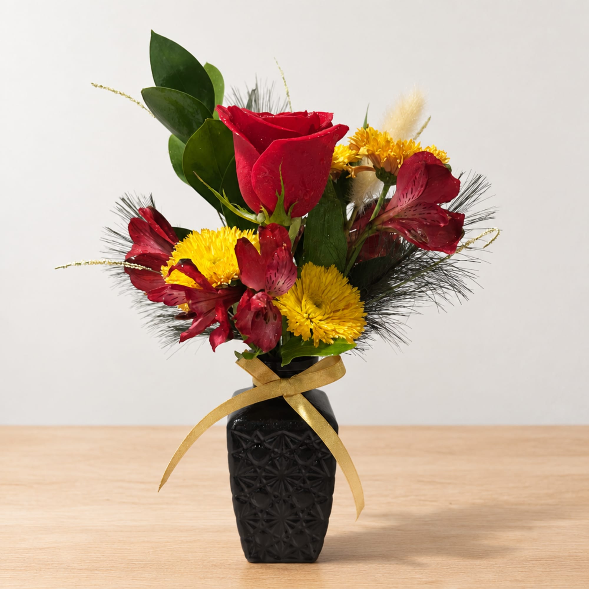Red roses and yellow flowers in a black vase with a gold ribbon
