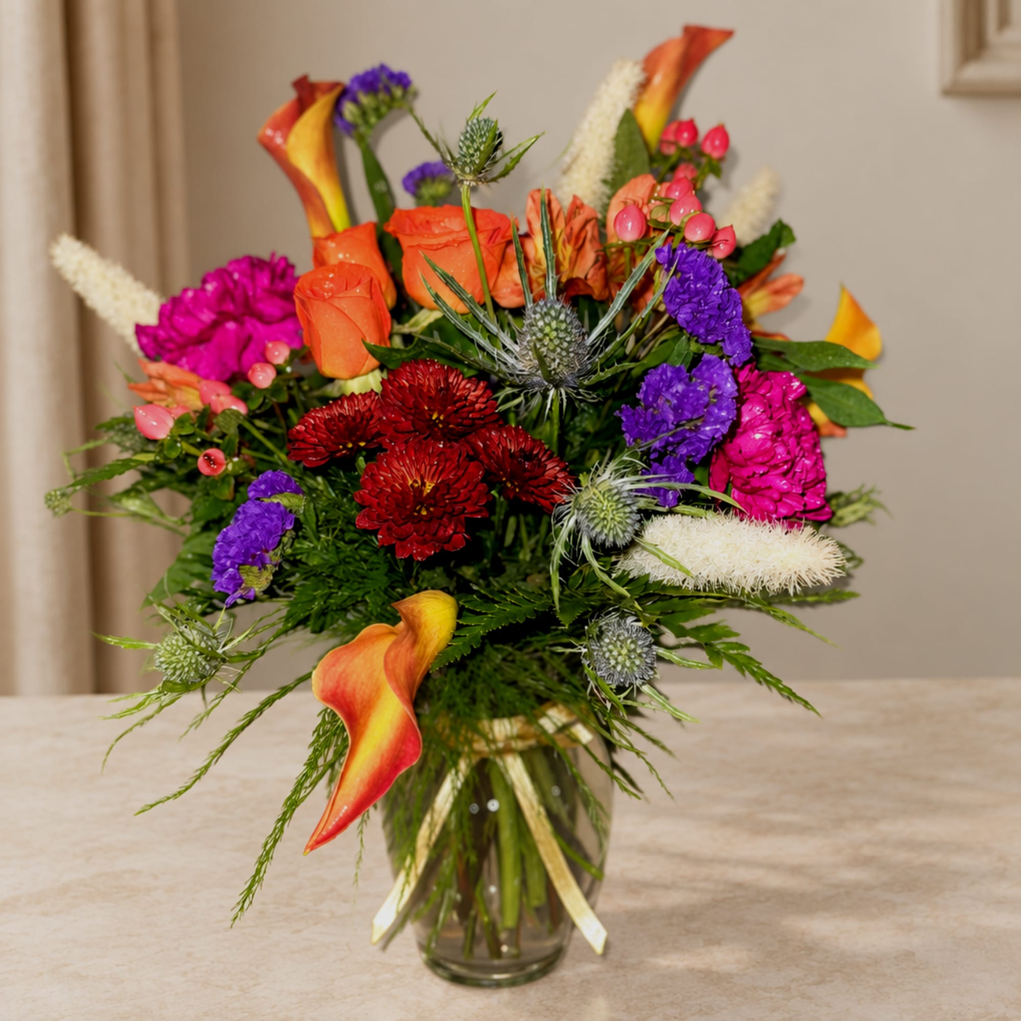 Colorful mixed bouquet in a glass vase with orange calla lilies and purple flowers