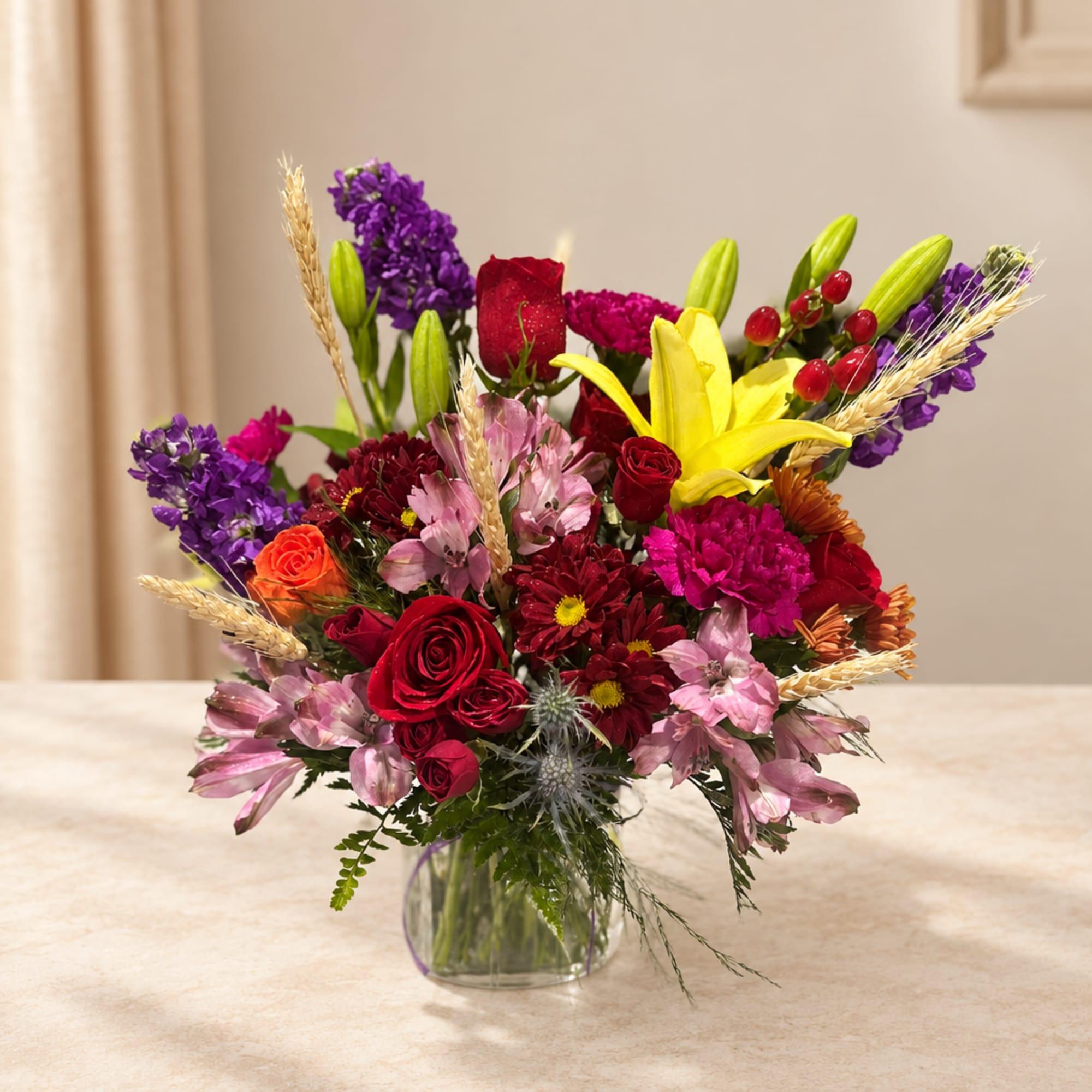 Mixed bouquet of roses, lilies, and purple flowers in a glass vase
