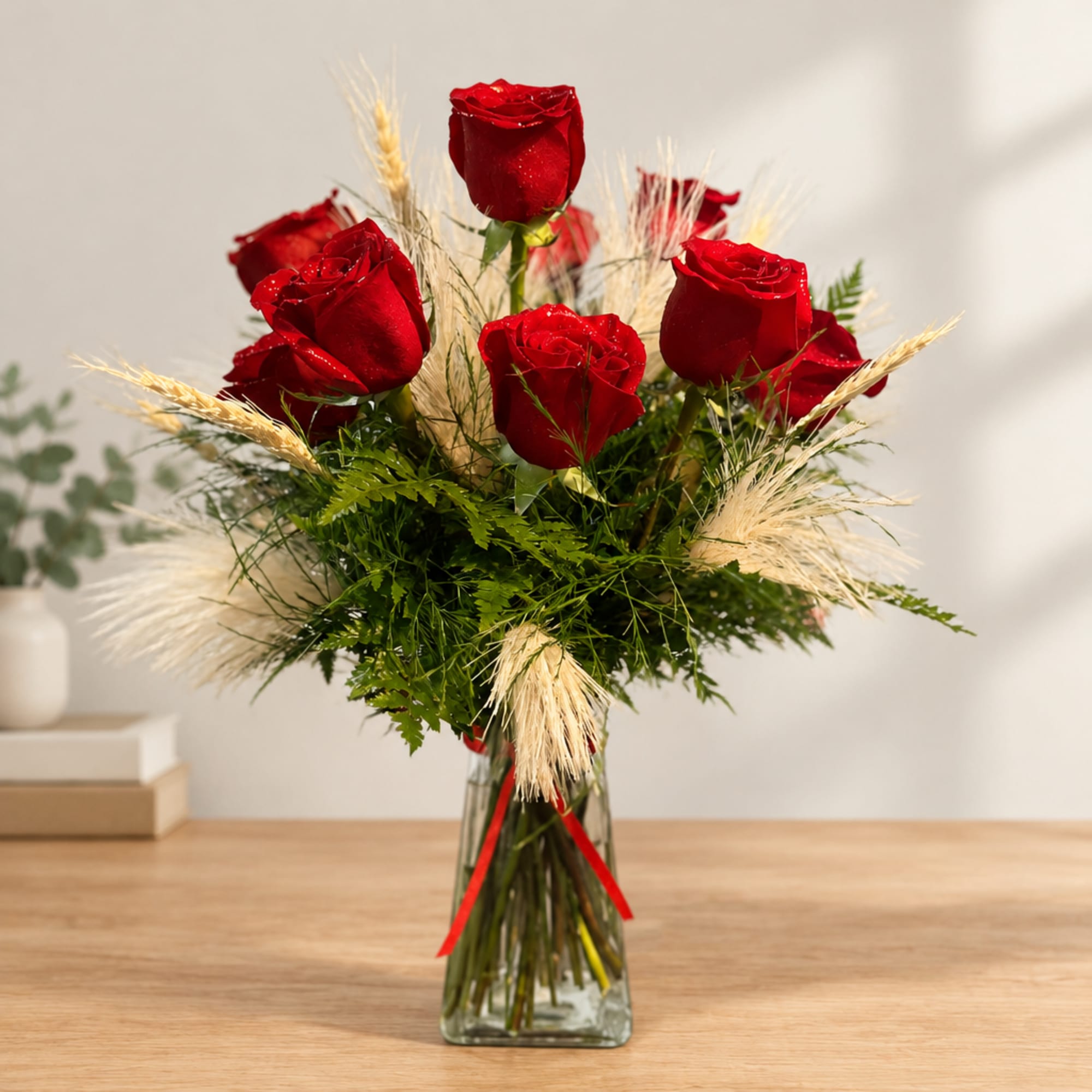 Red roses arranged in a clear glass vase with dried grass accents