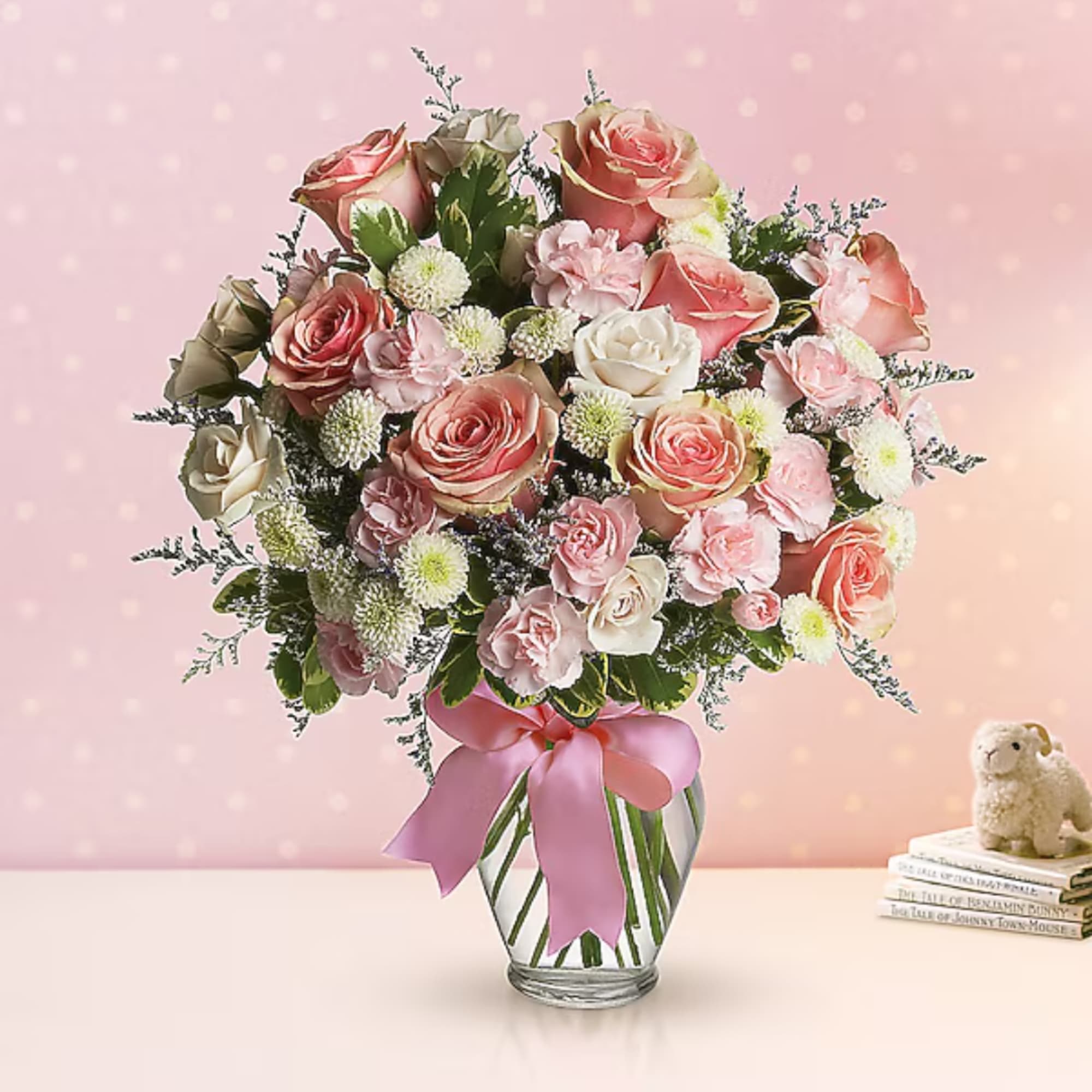 Pink and cream rose bouquet in a glass vase with a pink ribbon
