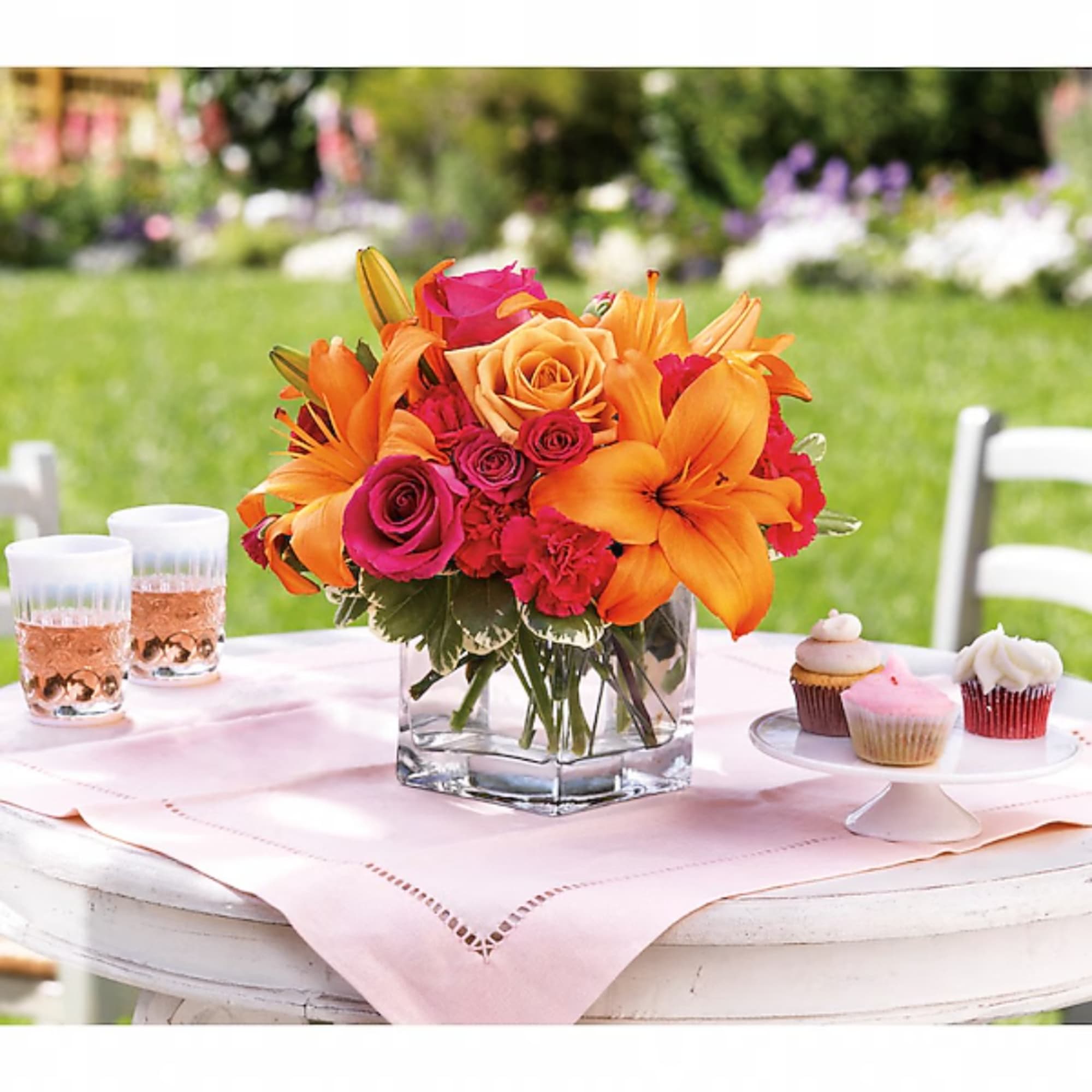 Orange and pink flower arrangement in a square glass vase on a table