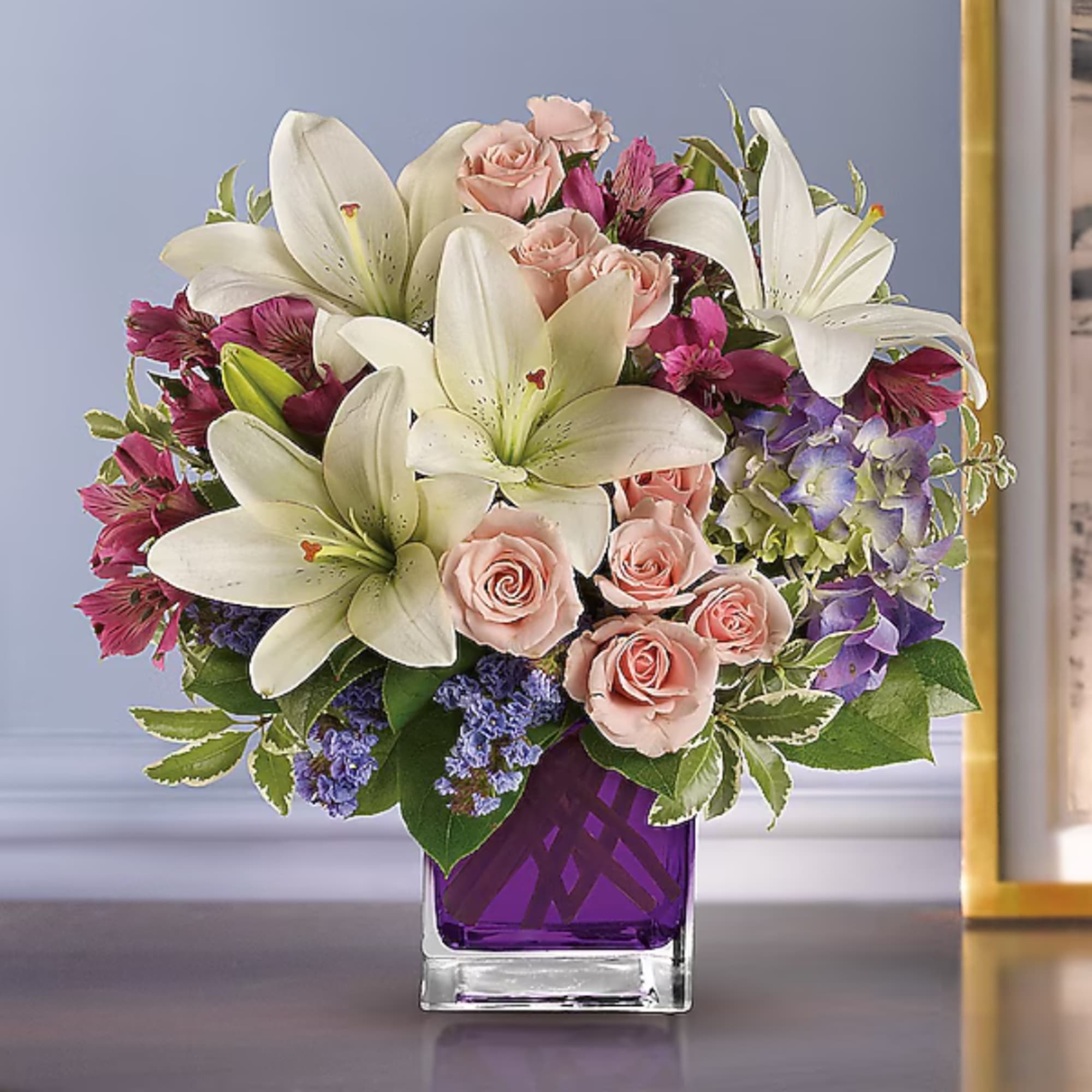 Bouquet of white lilies, pink roses, and purple flowers in a purple glass vase