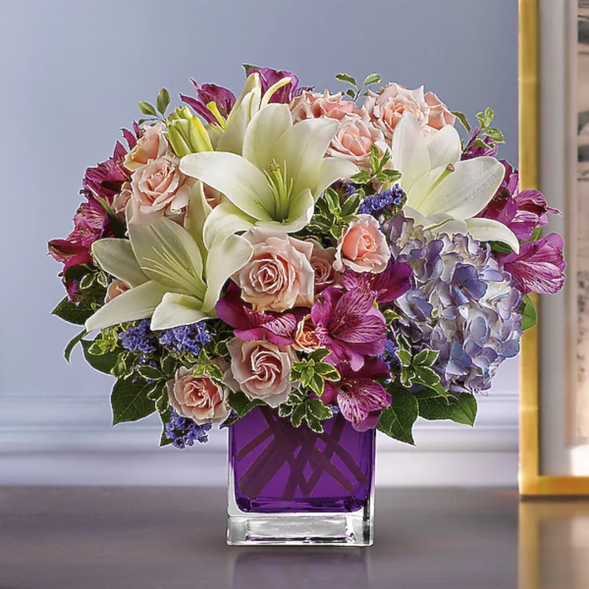 Bouquet of white lilies, pink roses, and purple flowers in a purple glass vase