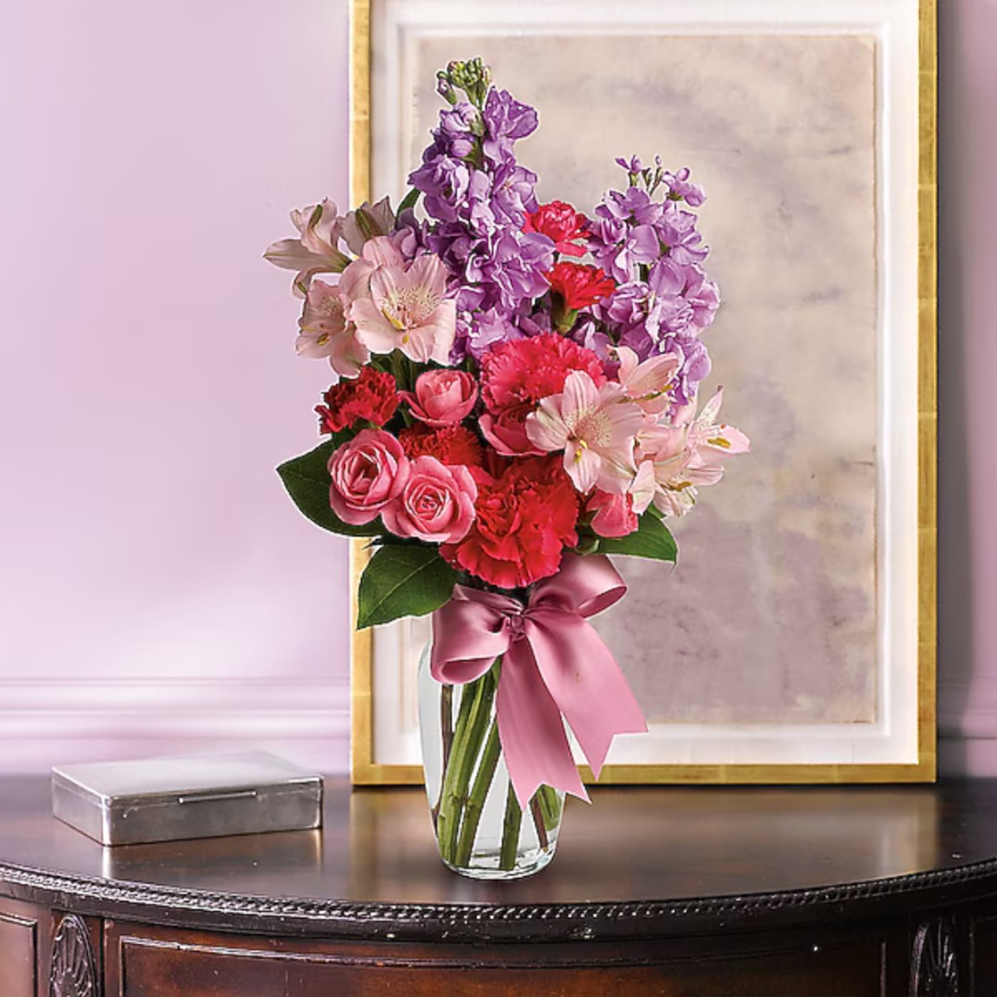 Pink and purple mixed flower bouquet in a glass vase with a satin ribbon