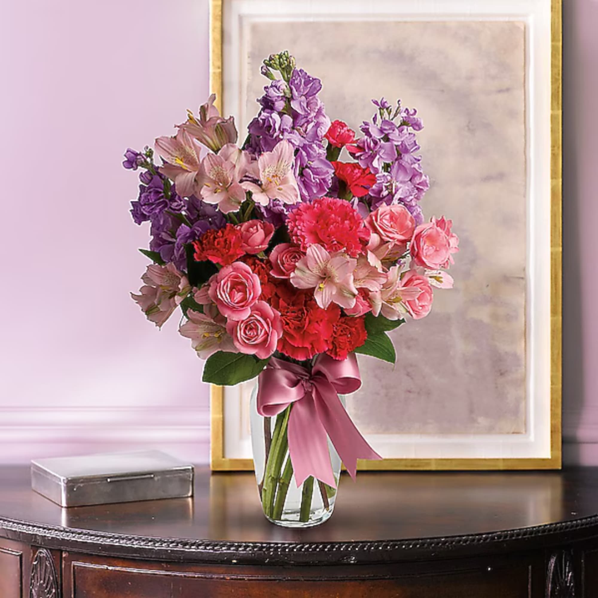 Pink and purple mixed bouquet in a clear glass vase with a ribbon