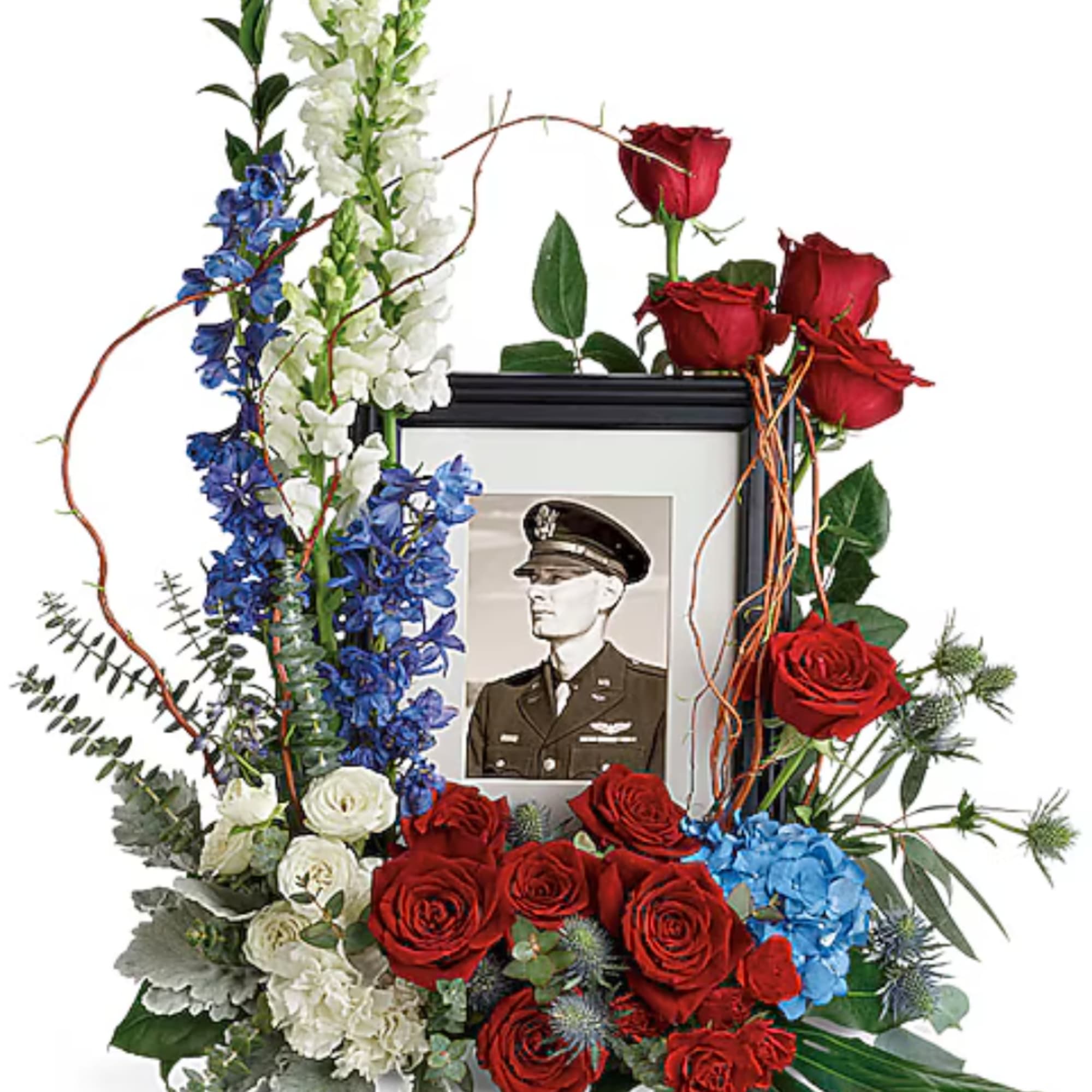 Floral tribute with red roses, blue and white flowers, and a framed portrait