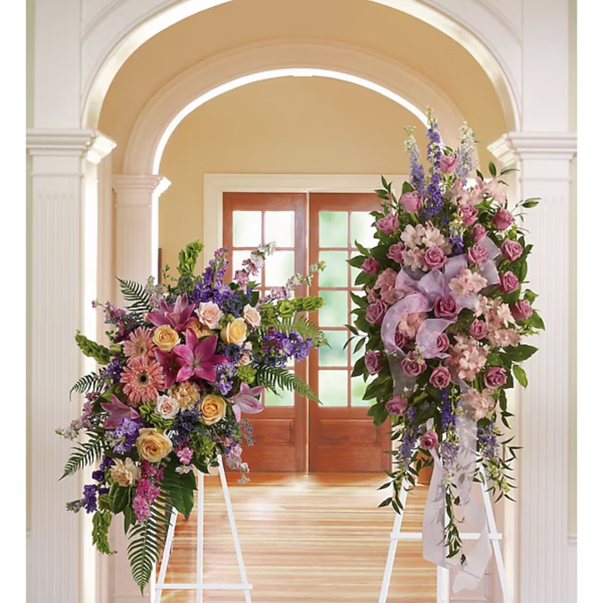 Two tall floral standing arrangements with pink, purple, and cream blooms on white easels