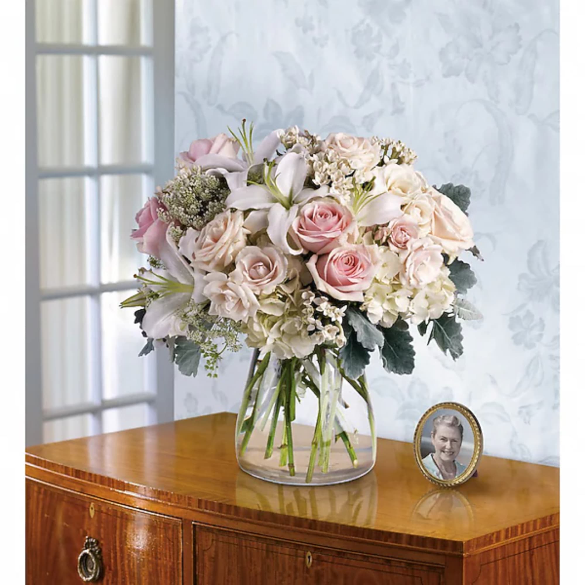 Blush roses and white lilies in a clear glass vase on a wooden table.