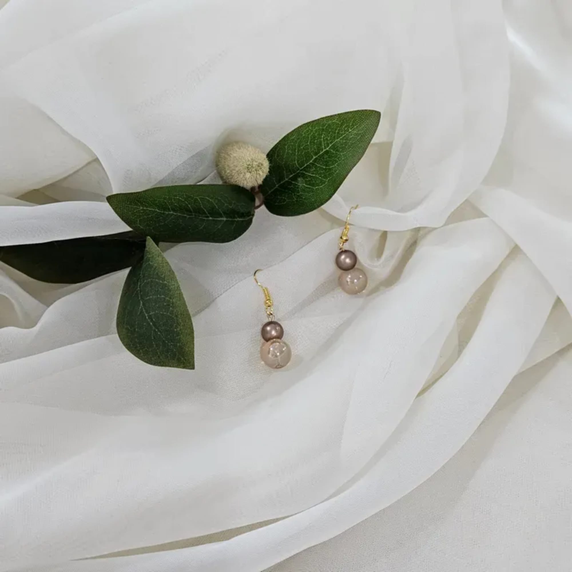 White fabric with green leaves and dangling pearl earrings