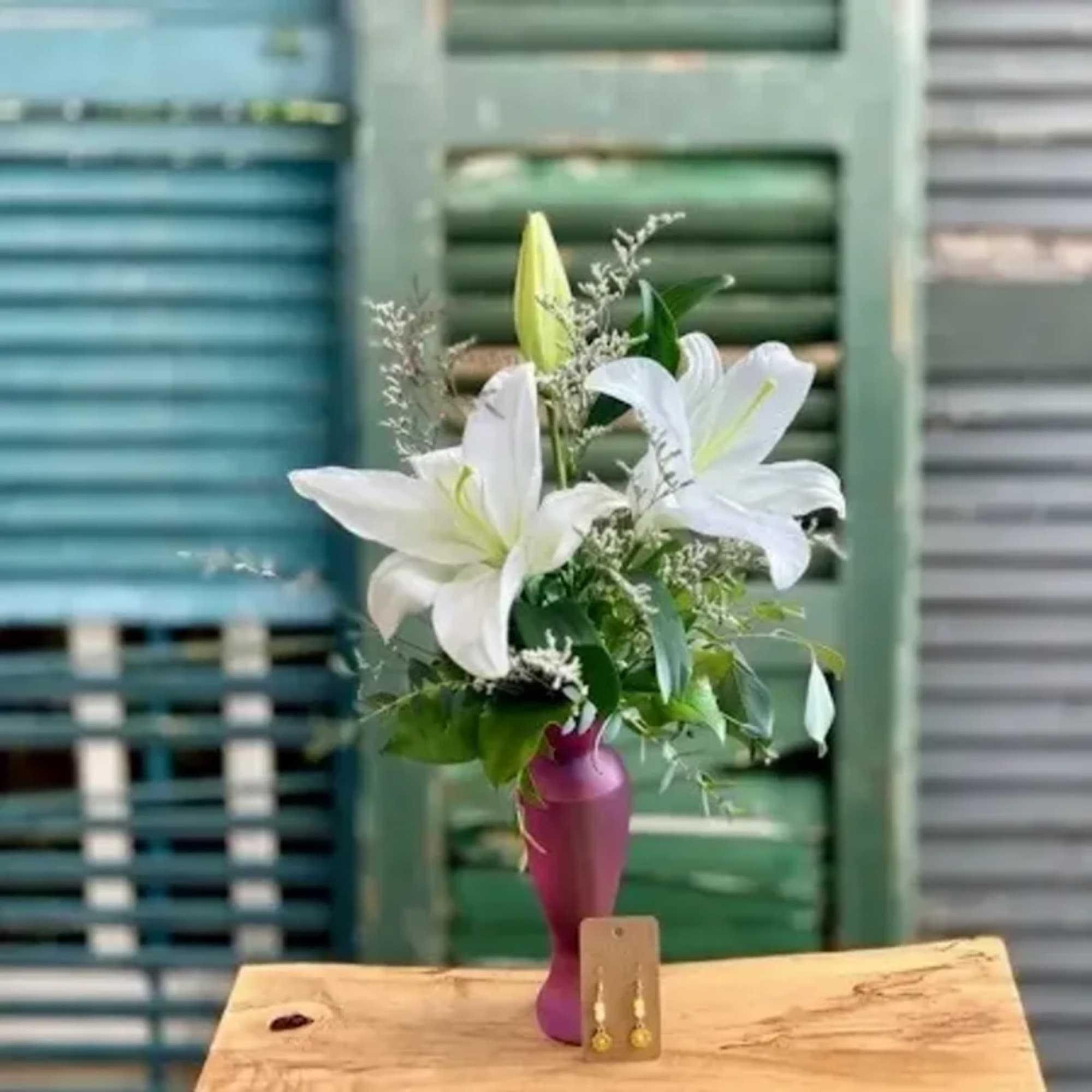 White lilies arranged in a purple vase with greenery