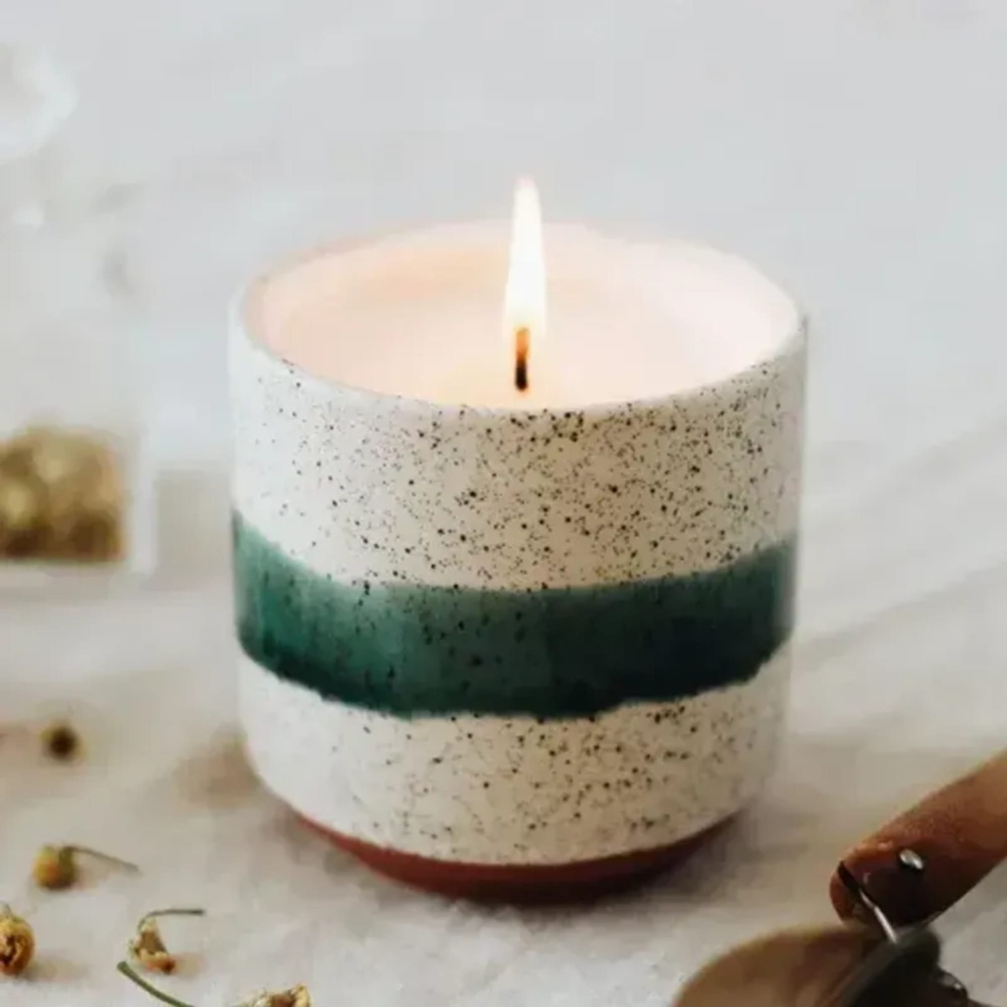 Lit speckled candle in a white container with a green band