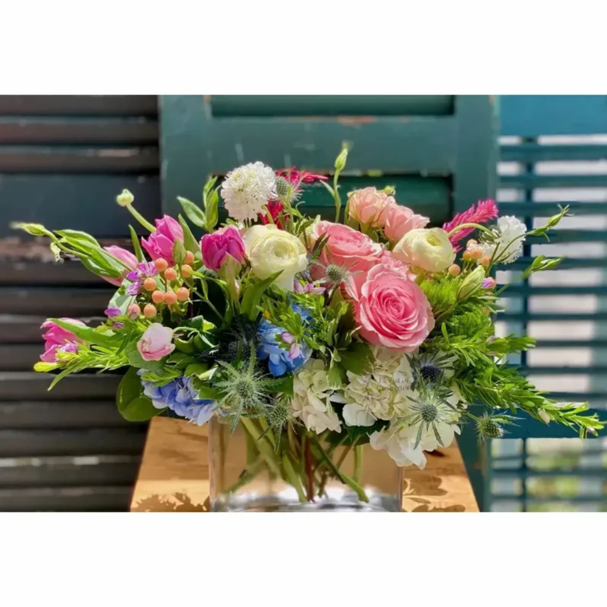 Mixed bouquet of pink, white, and blue flowers in a clear glass vase