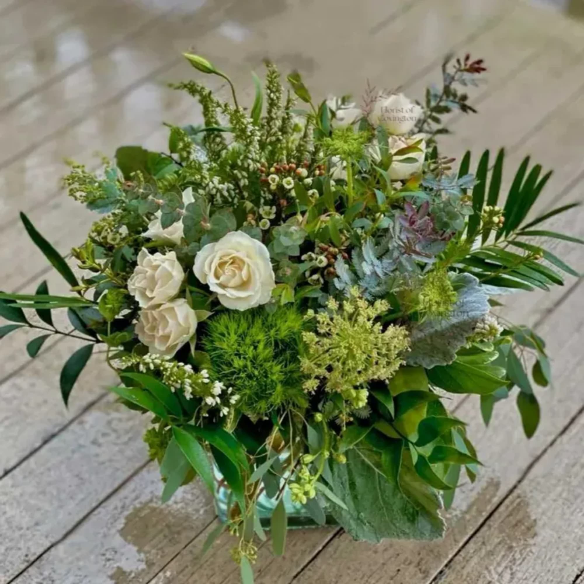 White roses and mixed greenery arranged in a glass vase