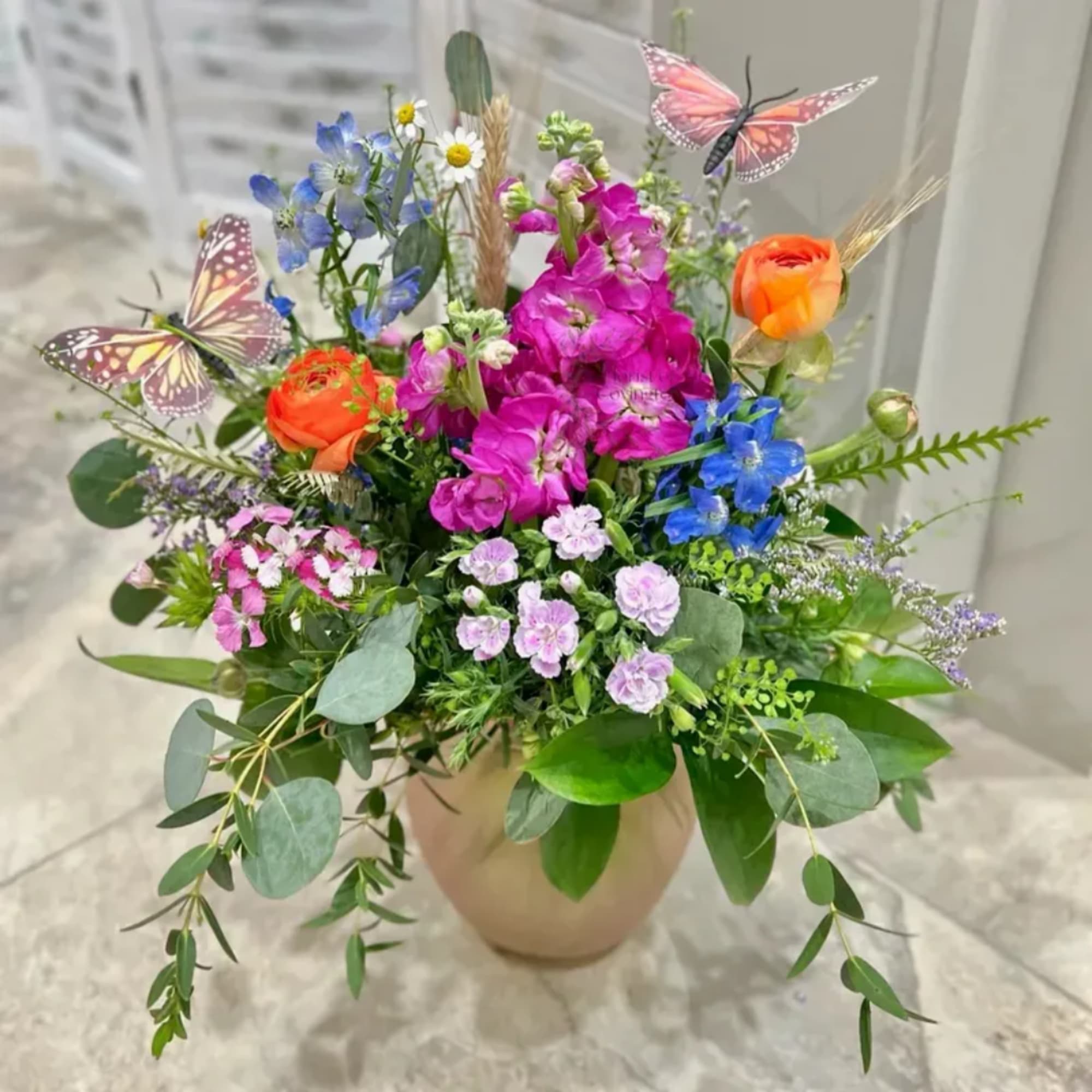 Mixed bouquet in a beige vase with orange, pink, blue, and lavender flowers