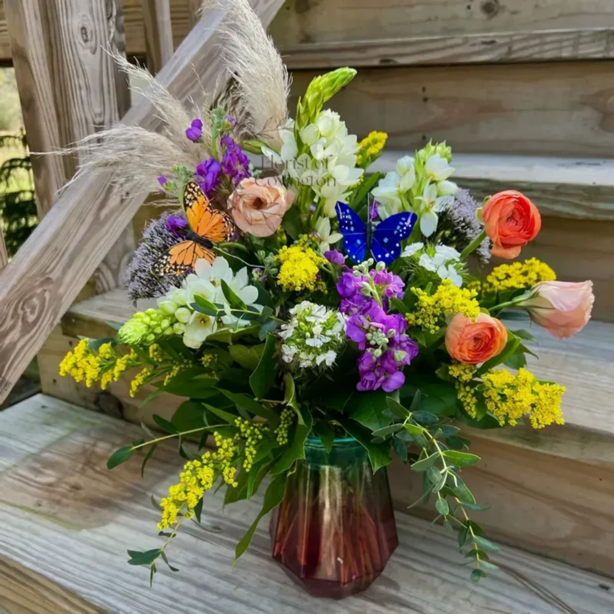 Mixed bouquet with orange, purple, white, and yellow flowers in a glass vase