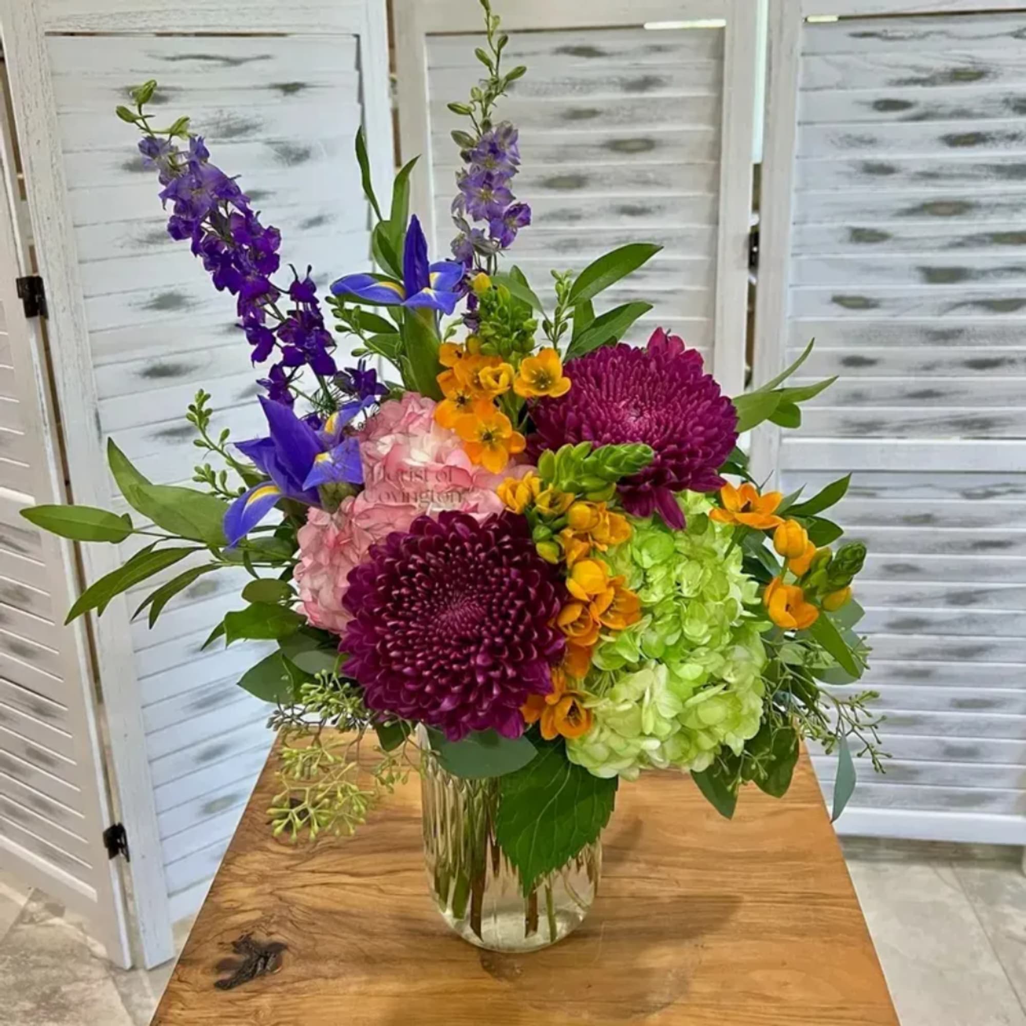 Colorful mixed bouquet in a clear glass vase with purple, pink, green, and orange blooms