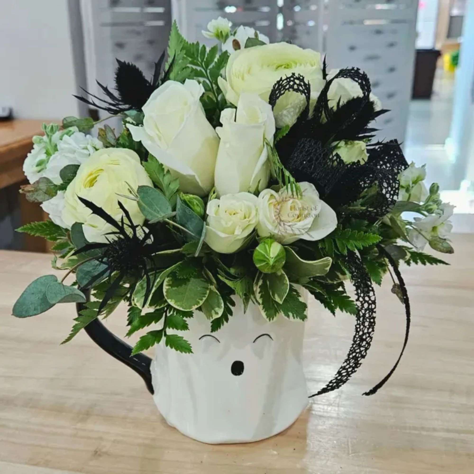 White roses and ranunculus arranged in a white mug-shaped vase