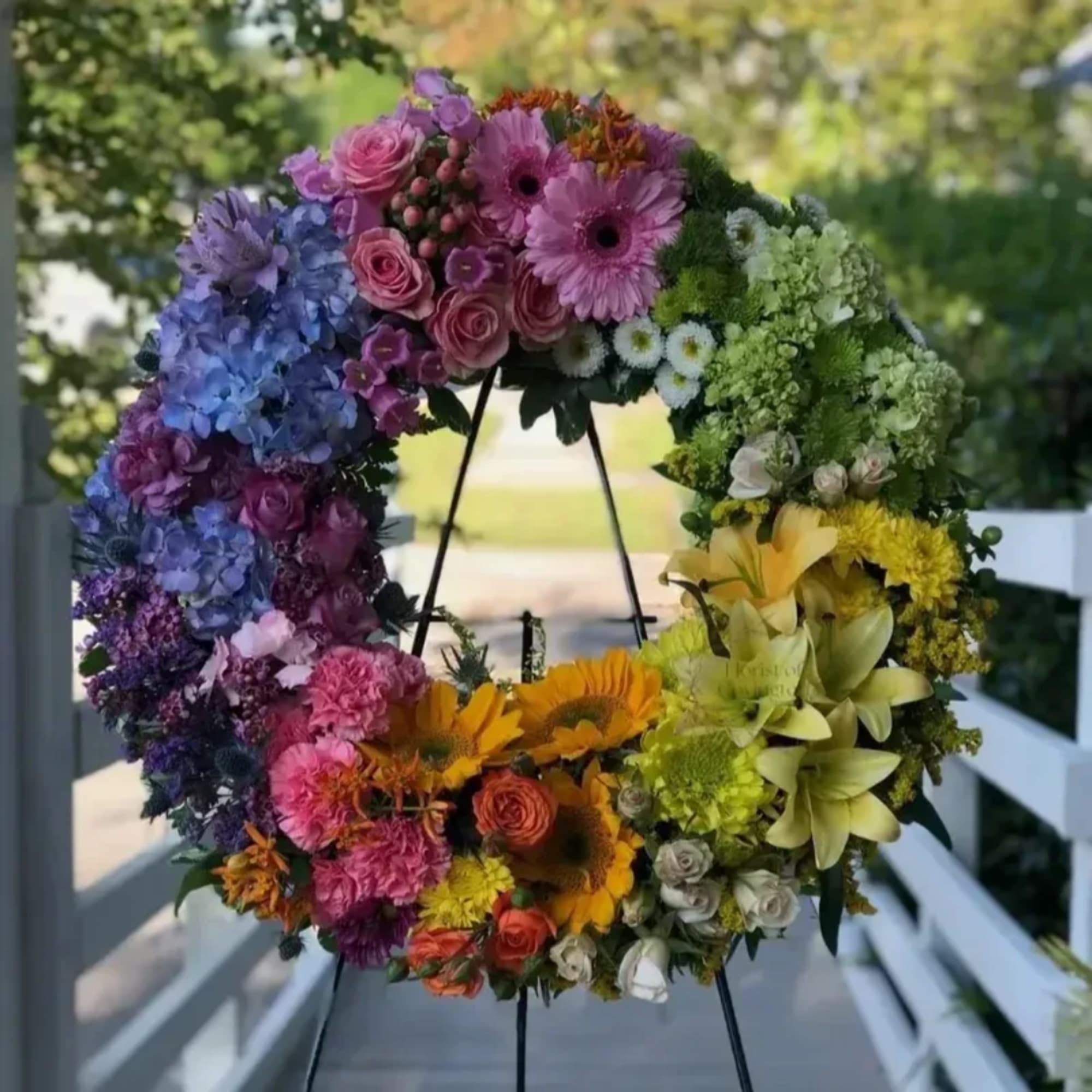 Colorful floral wreath on a black stand with roses, hydrangeas, and sunflowers
