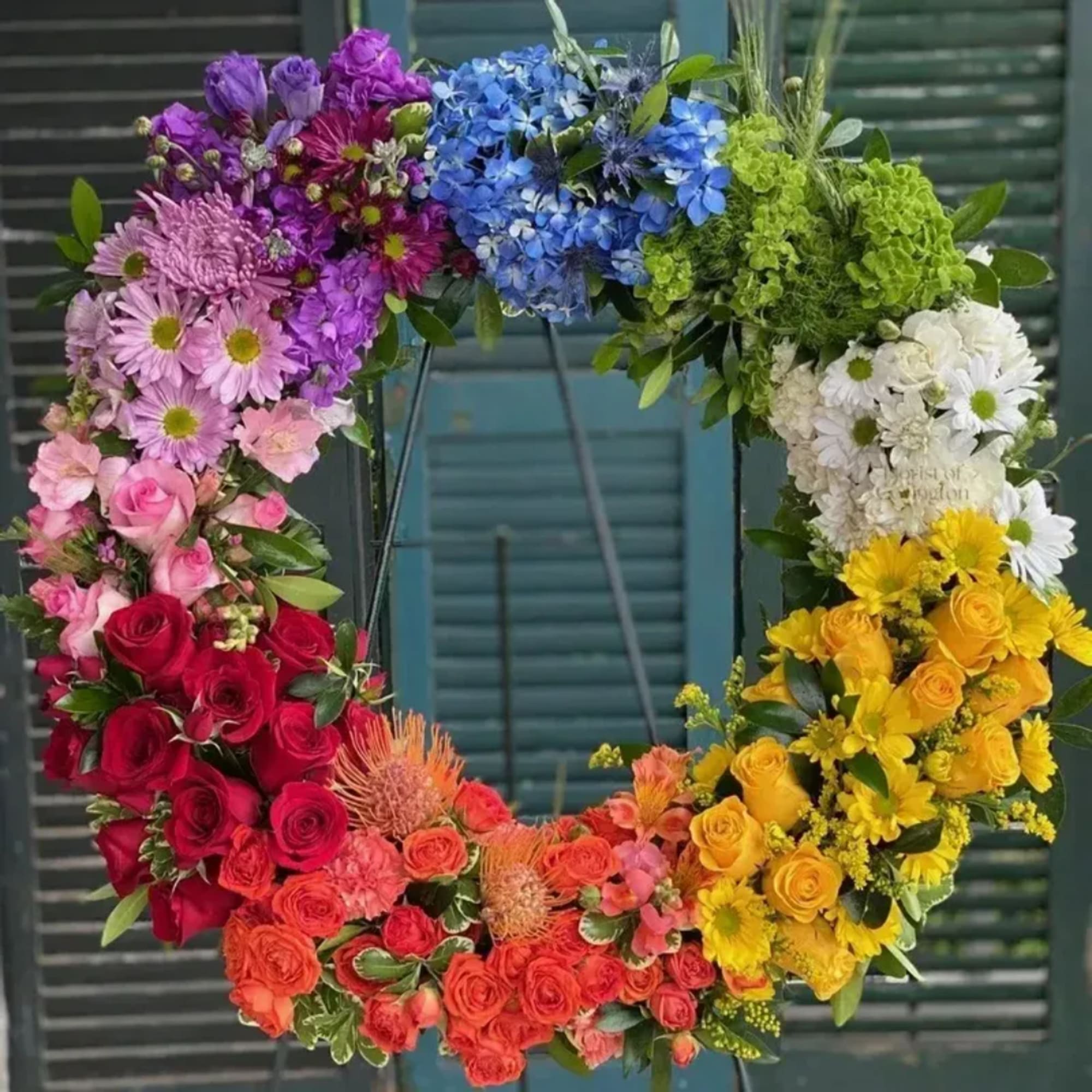 Colorful floral wreath with roses, daisies, and hydrangeas arranged in a rainbow circle