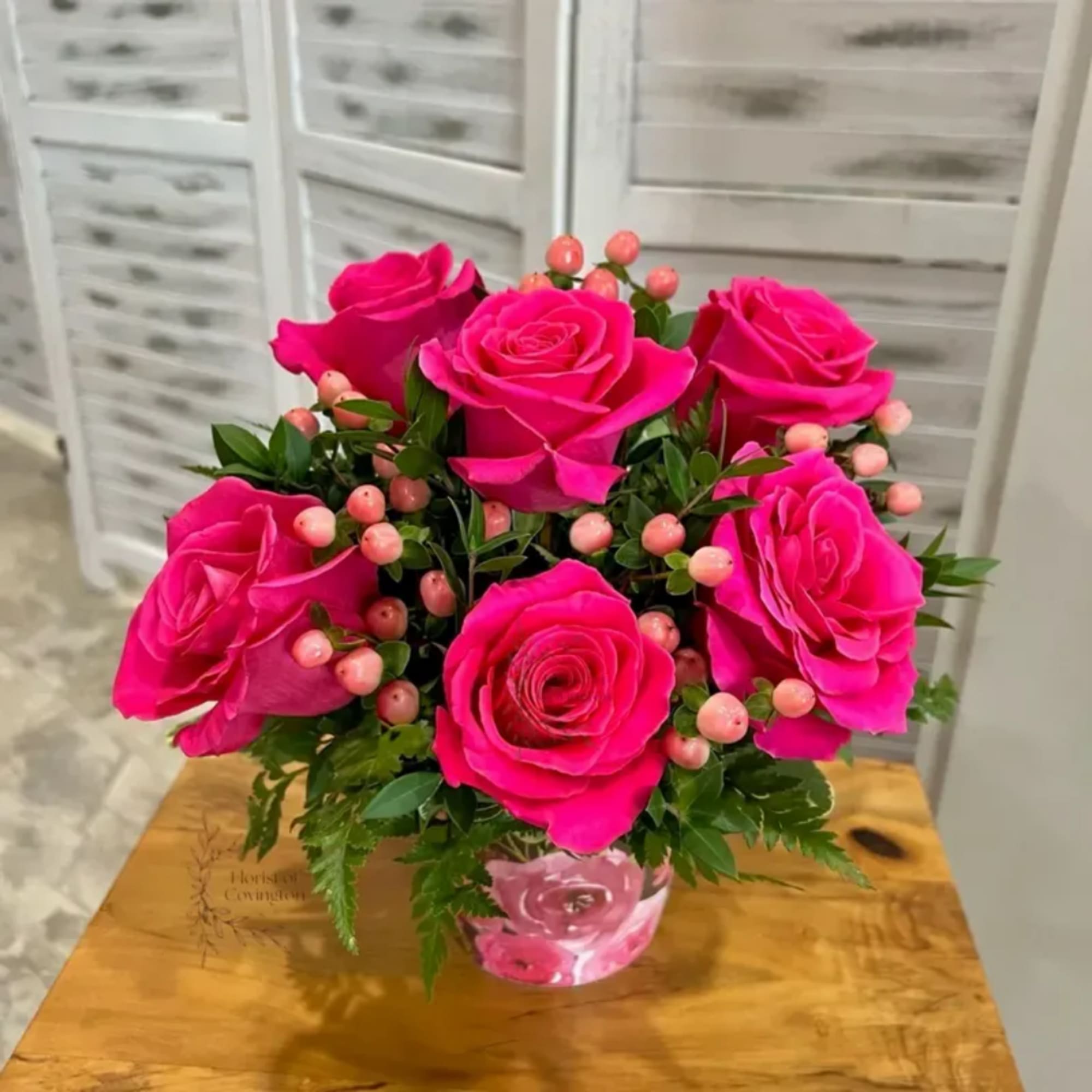 Hot pink roses arranged in a clear glass vase with pink berries