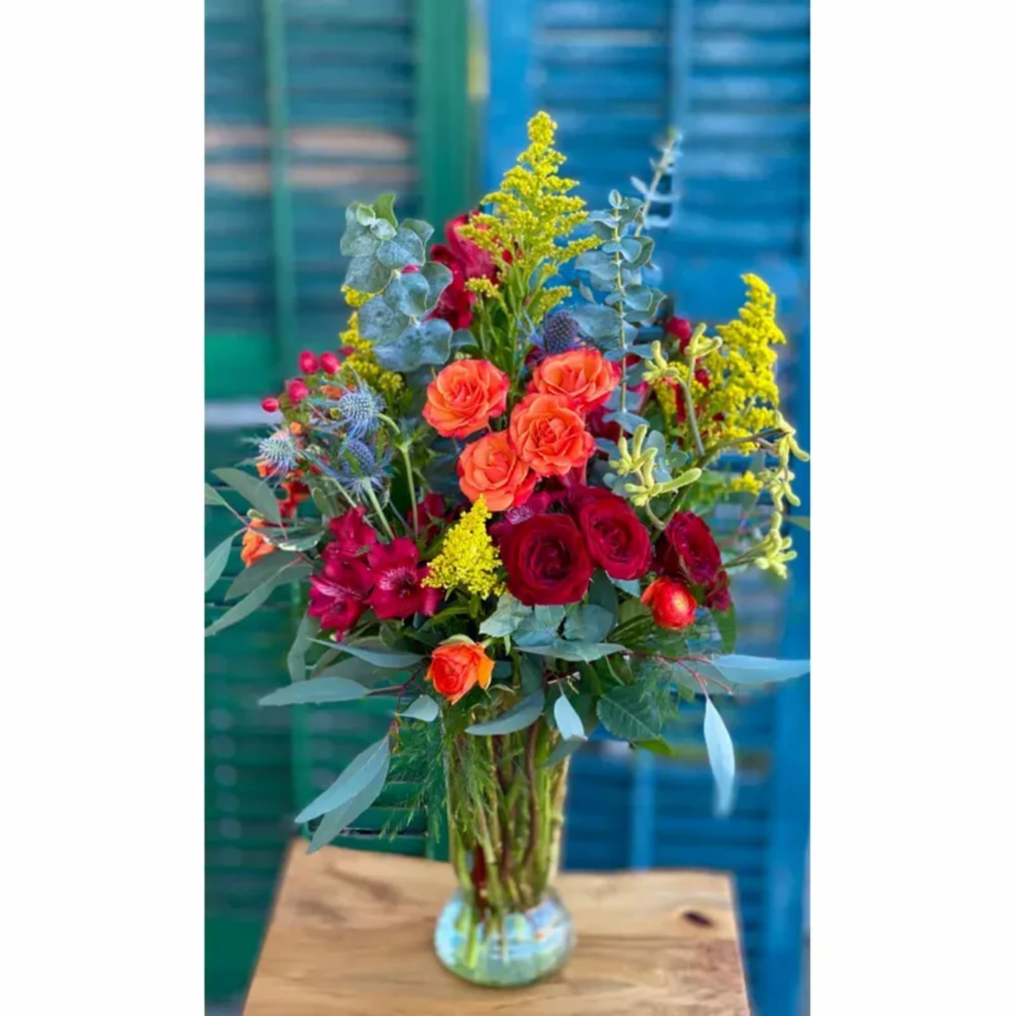 Tall mixed bouquet in a clear glass vase with orange and red roses