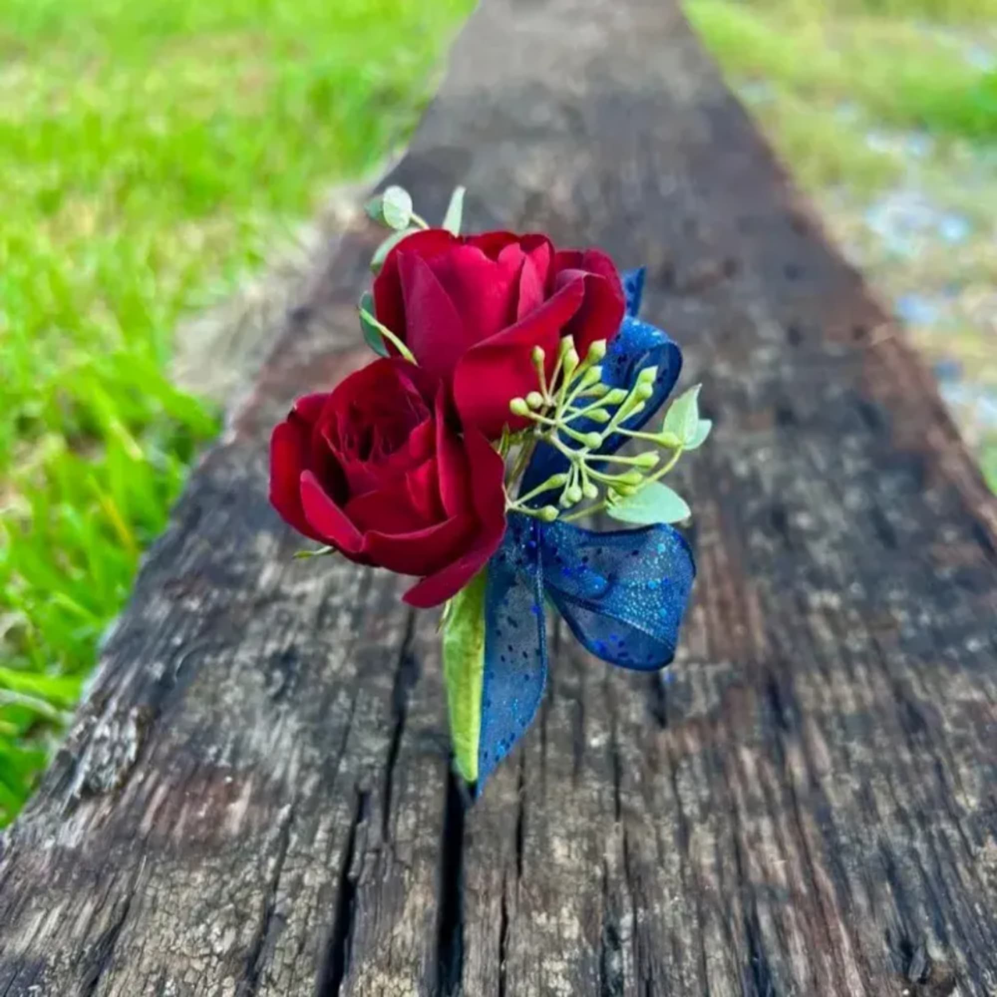 Red rose boutonniere with a blue ribbon on a wooden surface