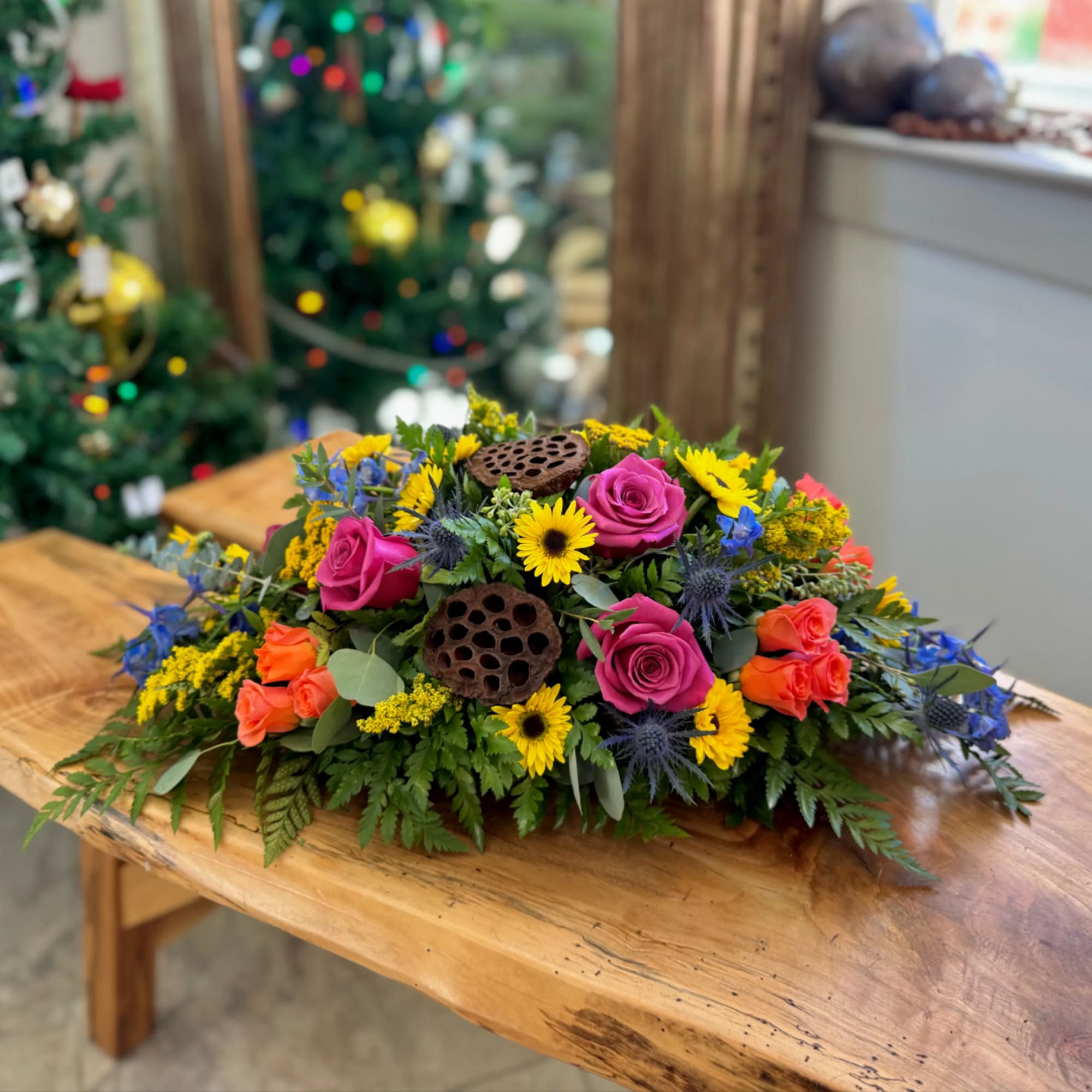 Low floral centerpiece with pink roses, yellow daisies, and blue accents