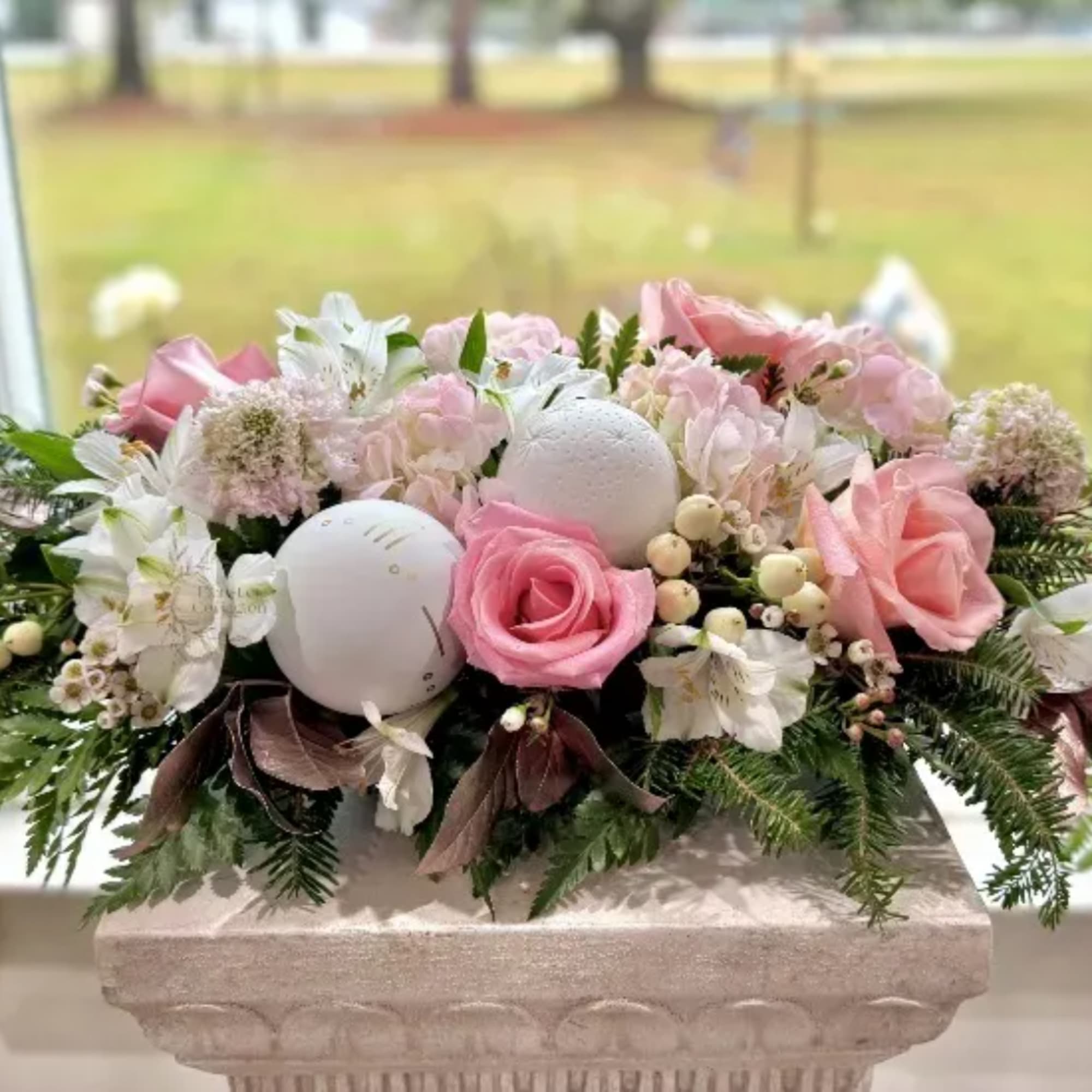 Pink roses and white flowers arranged in a low stone planter with decorative spheres