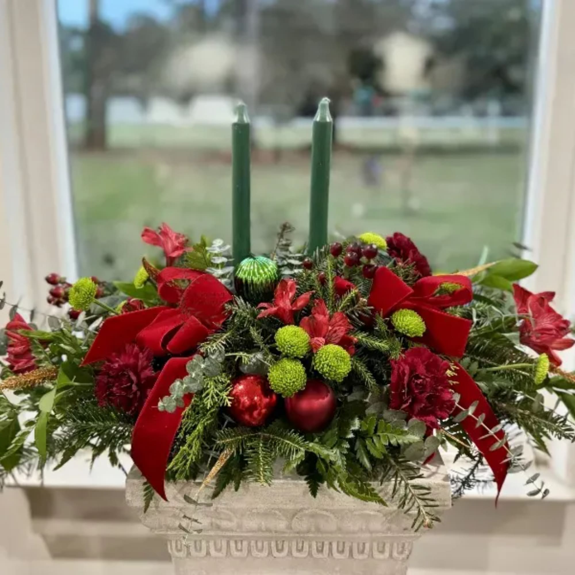 Christmas centerpiece with red flowers, green candles, and a stone planter