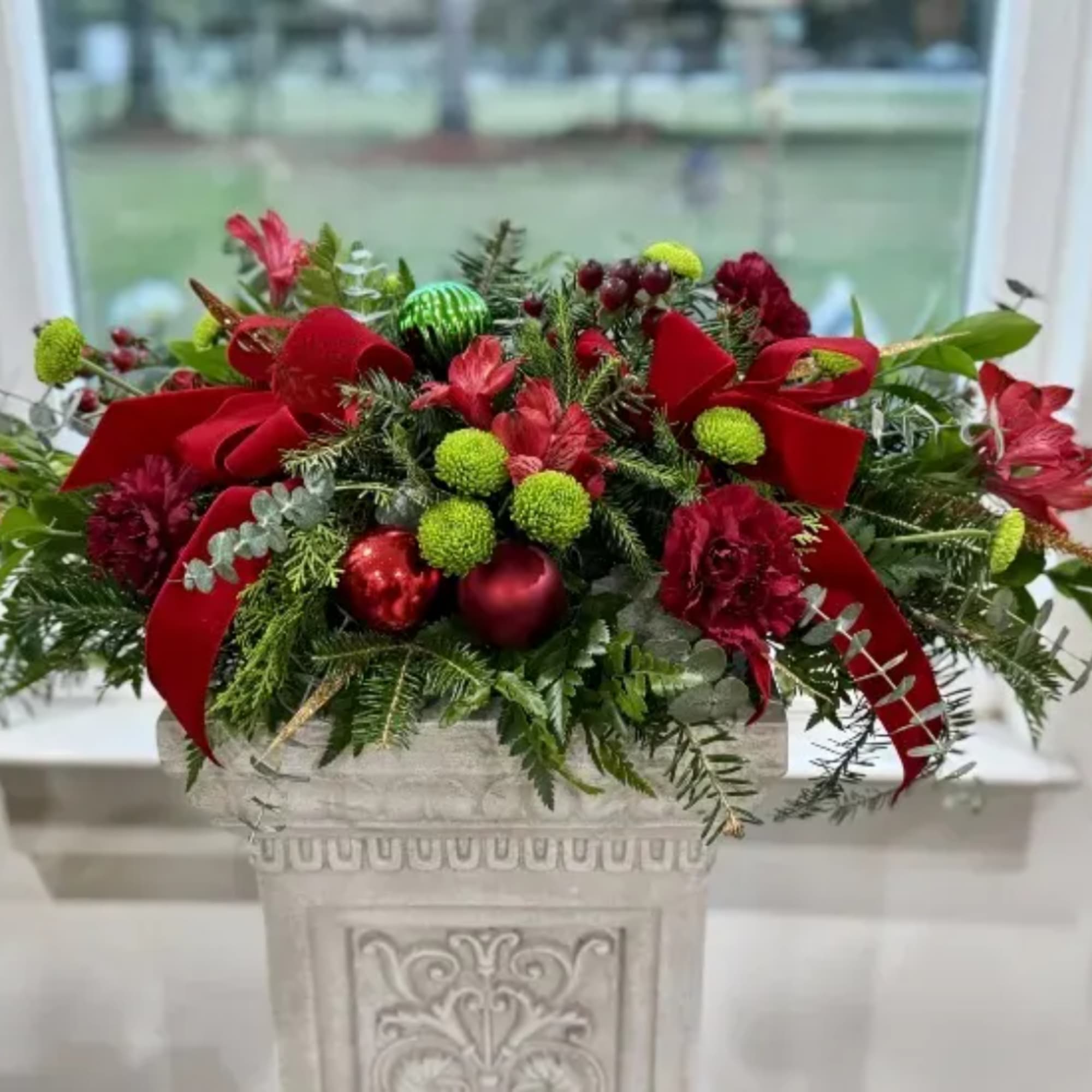 Christmas arrangement in a decorative stone planter with red ribbons and ornaments