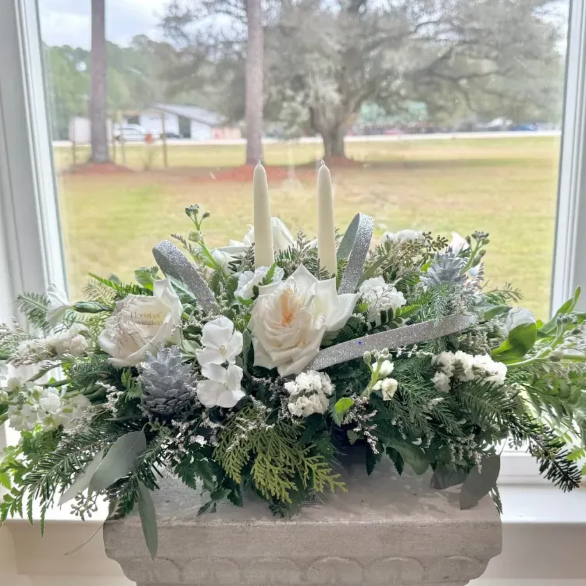 White floral centerpiece with candles and silver ribbon in a stone planter