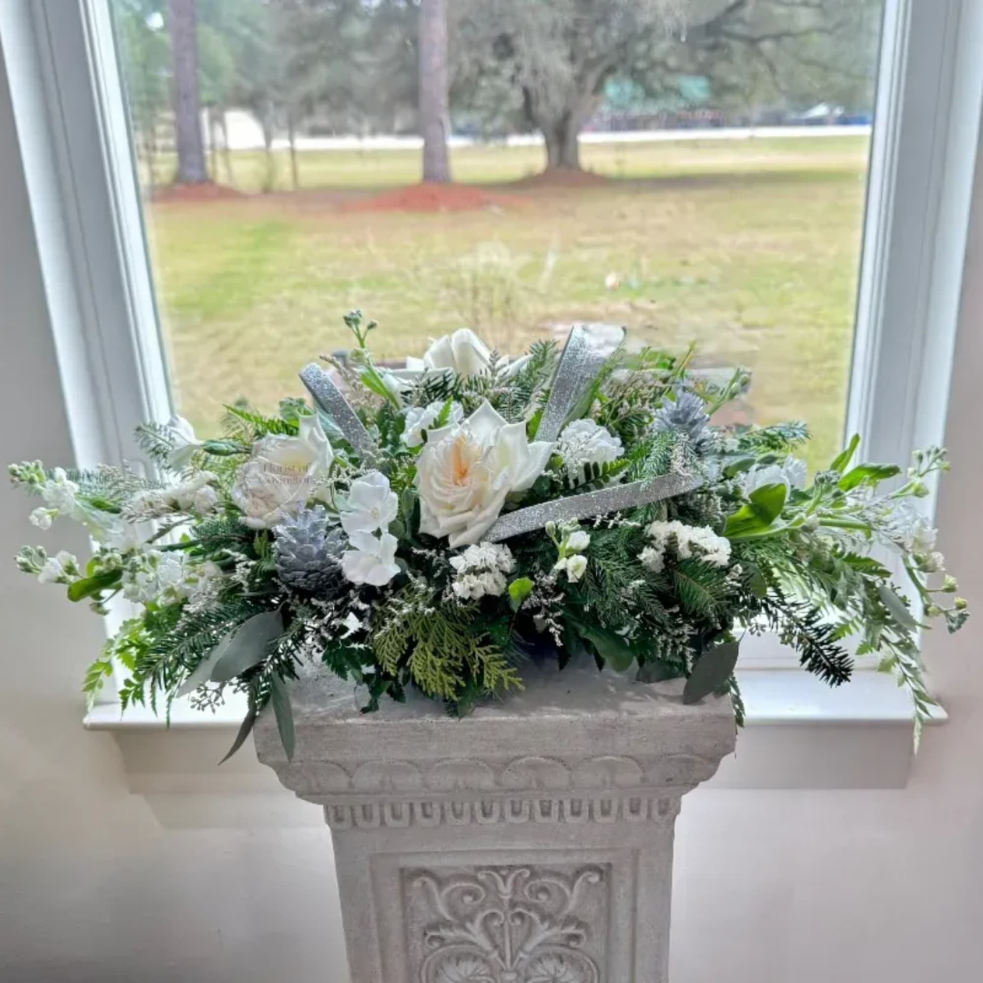 White floral arrangement in a stone planter with silver ribbon accents