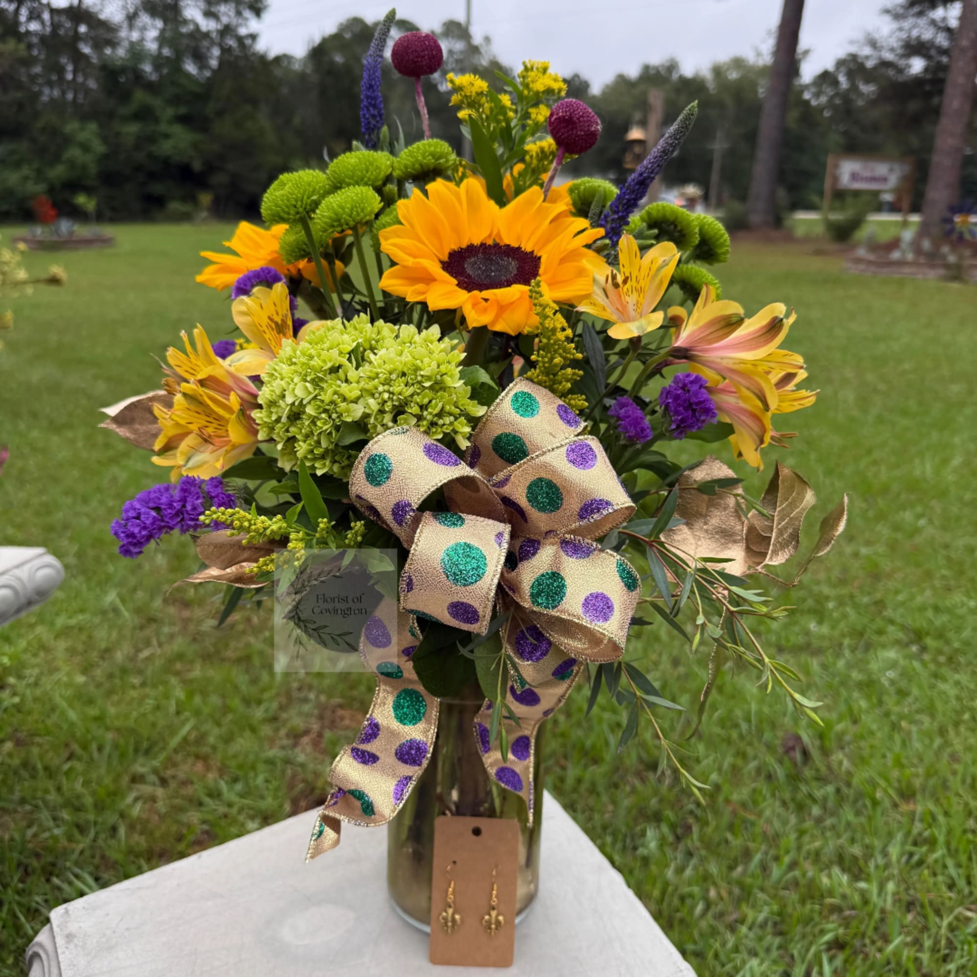 Bouquet with sunflowers, yellow alstroemeria, and purple accents in a glass vase.