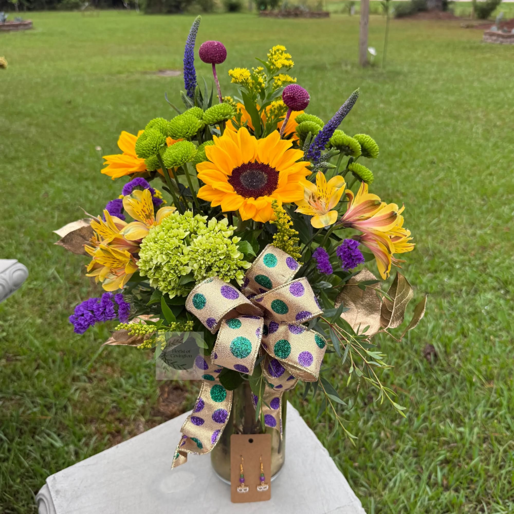 Colorful bouquet with sunflowers, purple blooms, and a polka-dot ribbon in a vase.